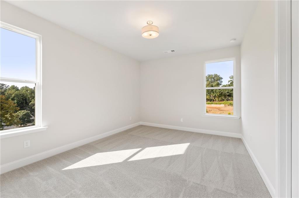 Bright bedroom with white walls, large windows overlooking trees, and sunlit gray carpet in Davidson Homes The Hampton C, Buford, GA