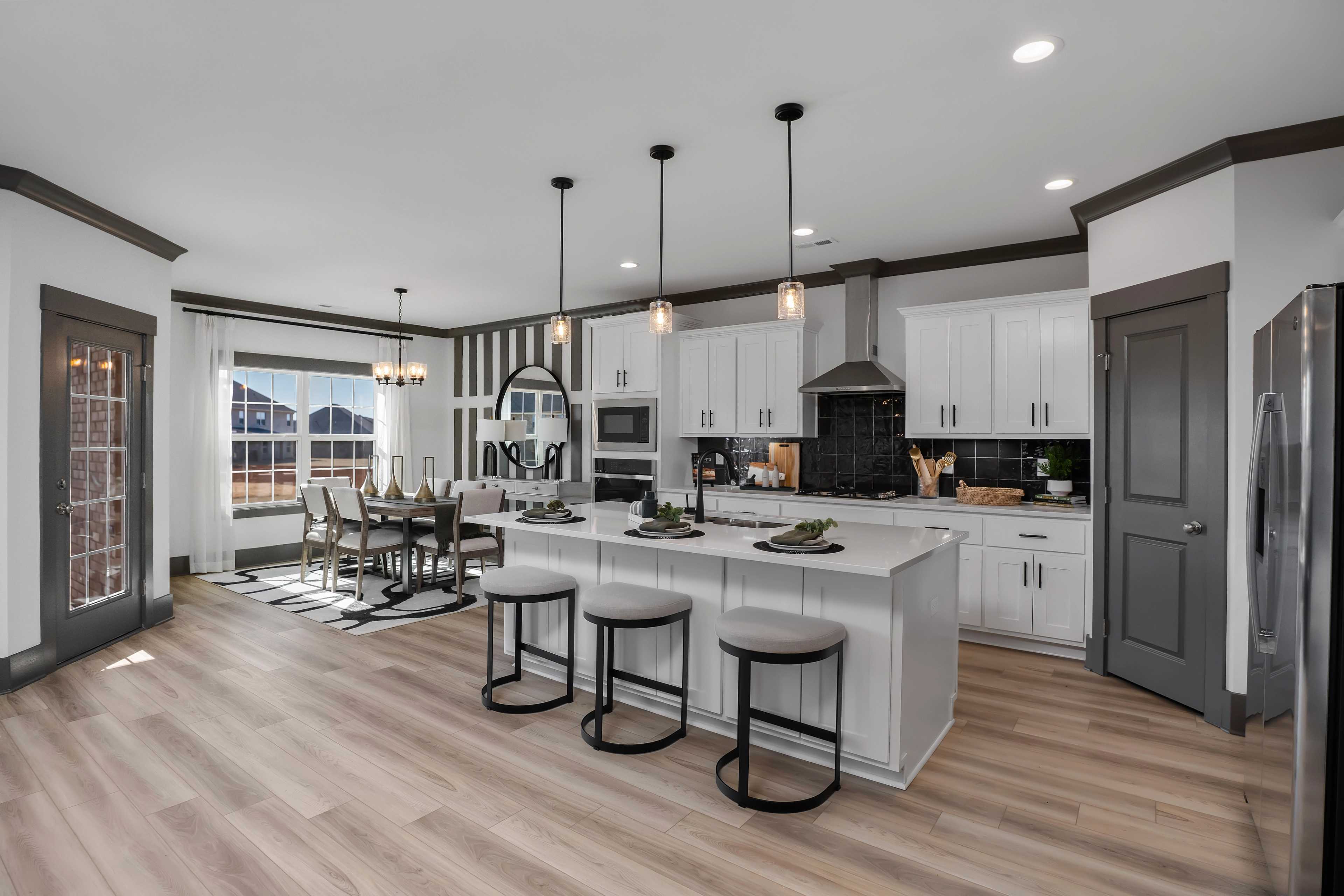 Open-concept kitchen dining area at Barnett's Crossing in Madison Alabama with white cabinets island bar stools hardwood floors pendant lights