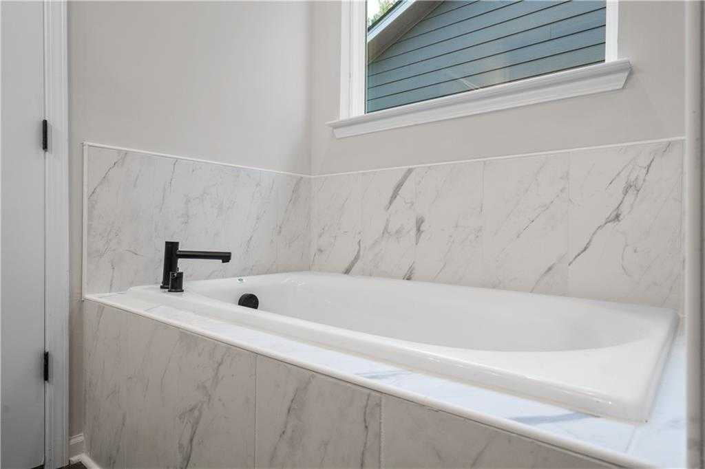 Luxurious master bath with white marble surround soaking tub, black faucet, and large window in Davidson Homes The Daphne B, Loganville, GA