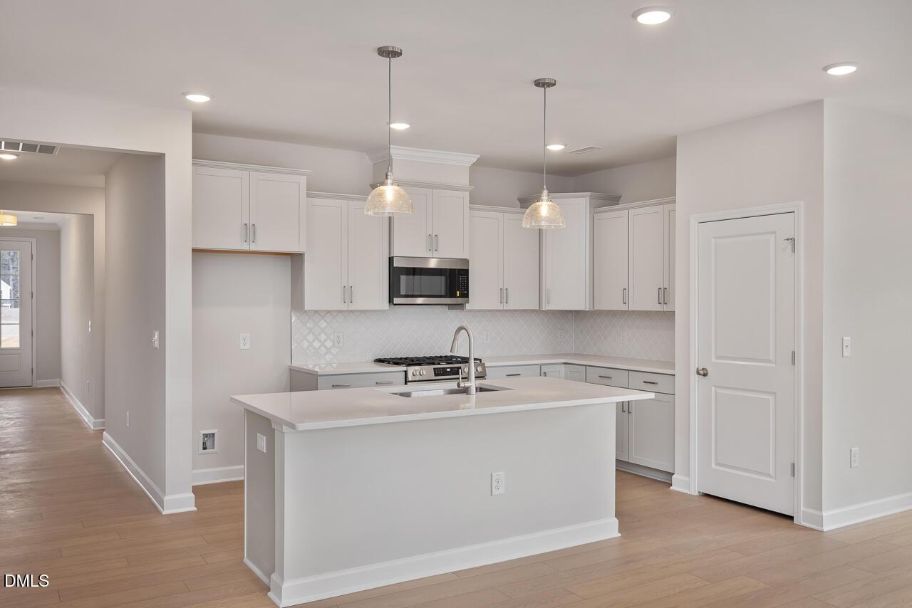 Modern white kitchen with large island, stainless appliances, pendant lights in The Daphne C by Davidson Homes, Zebulon, NC