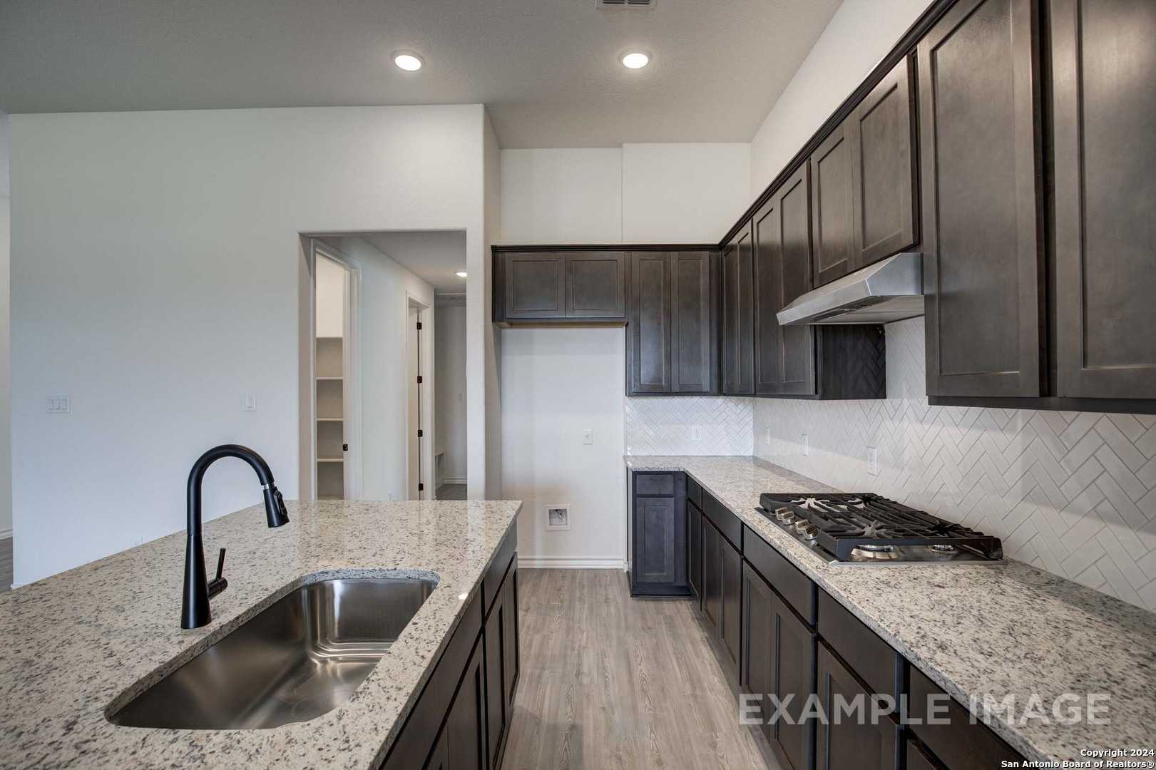 Modern kitchen with dark shaker cabinets, granite island sink, subway tile backsplash in The Garner C floor plan, Castroville, TX