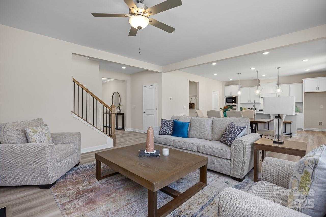 Open-concept living room with beige sectional sofa, wood coffee table, and ceiling fan open to white kitchen in Davidson Homes The Chestnut F, Belmont, NC