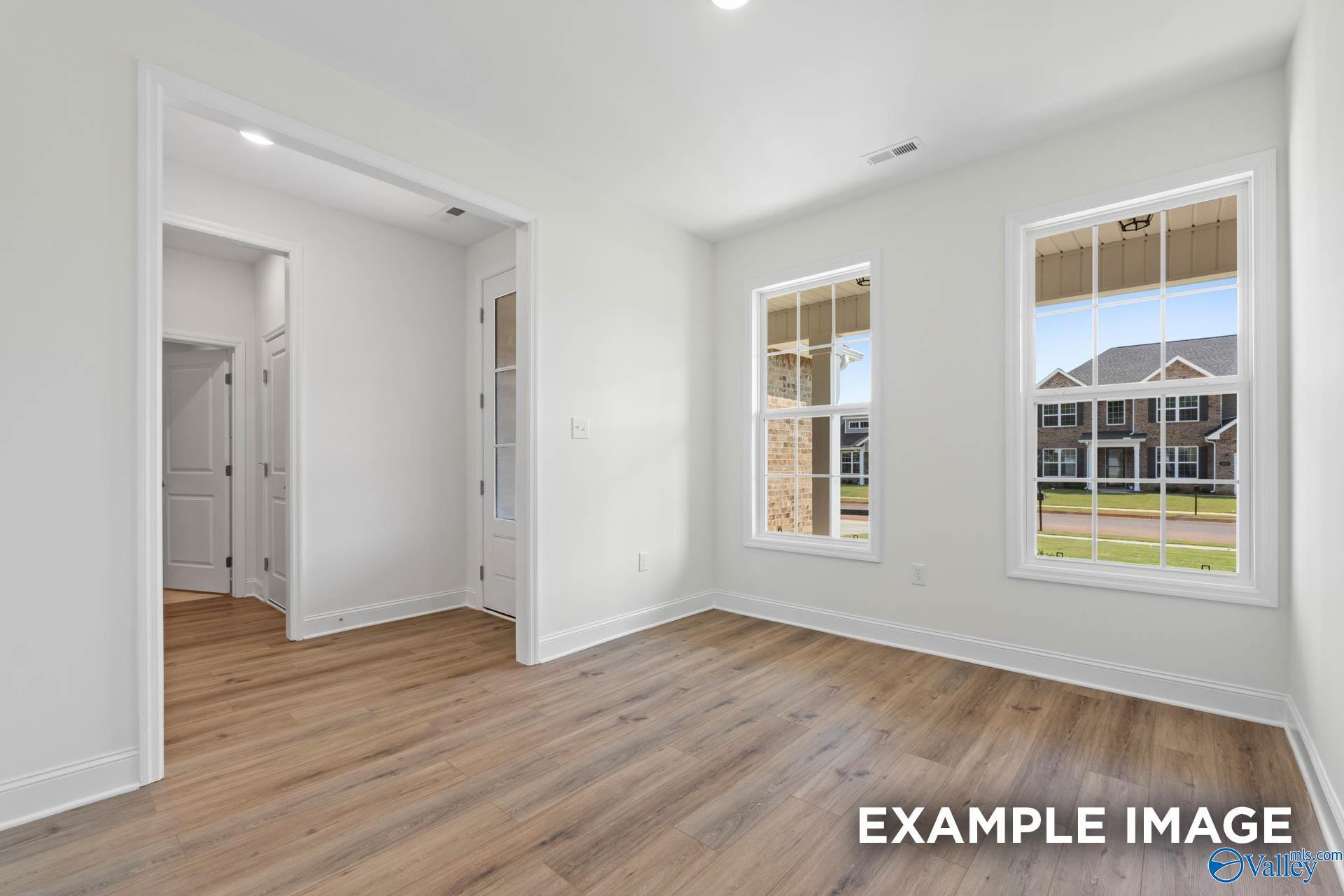 Bright empty room with hardwood floors, white walls, and large windows overlooking neighborhood in Davidson Homes The Rockford C, Madison, Alabama