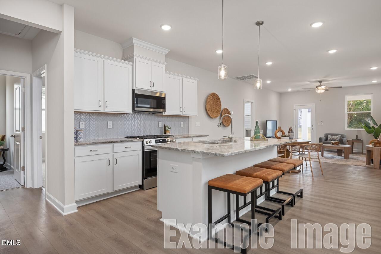 Modern open-concept kitchen with white shaker cabinets, stainless appliances, quartz island, and bar stools in Davidson Homes The Carter C, Lillington, NC