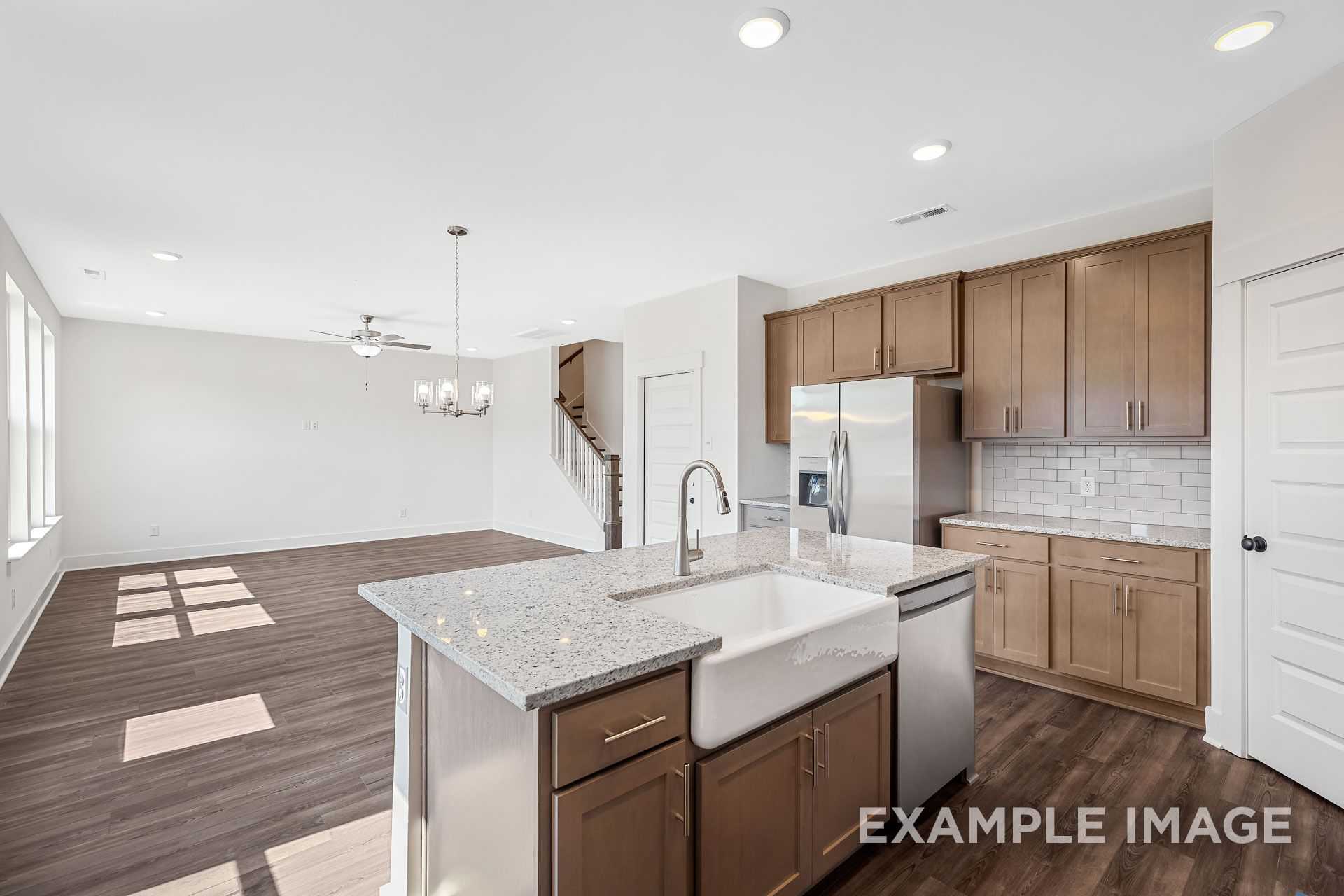 Open-concept kitchen in The Logan B featuring granite island with farmhouse sink, wood cabinets, stainless appliances, and sunny living space