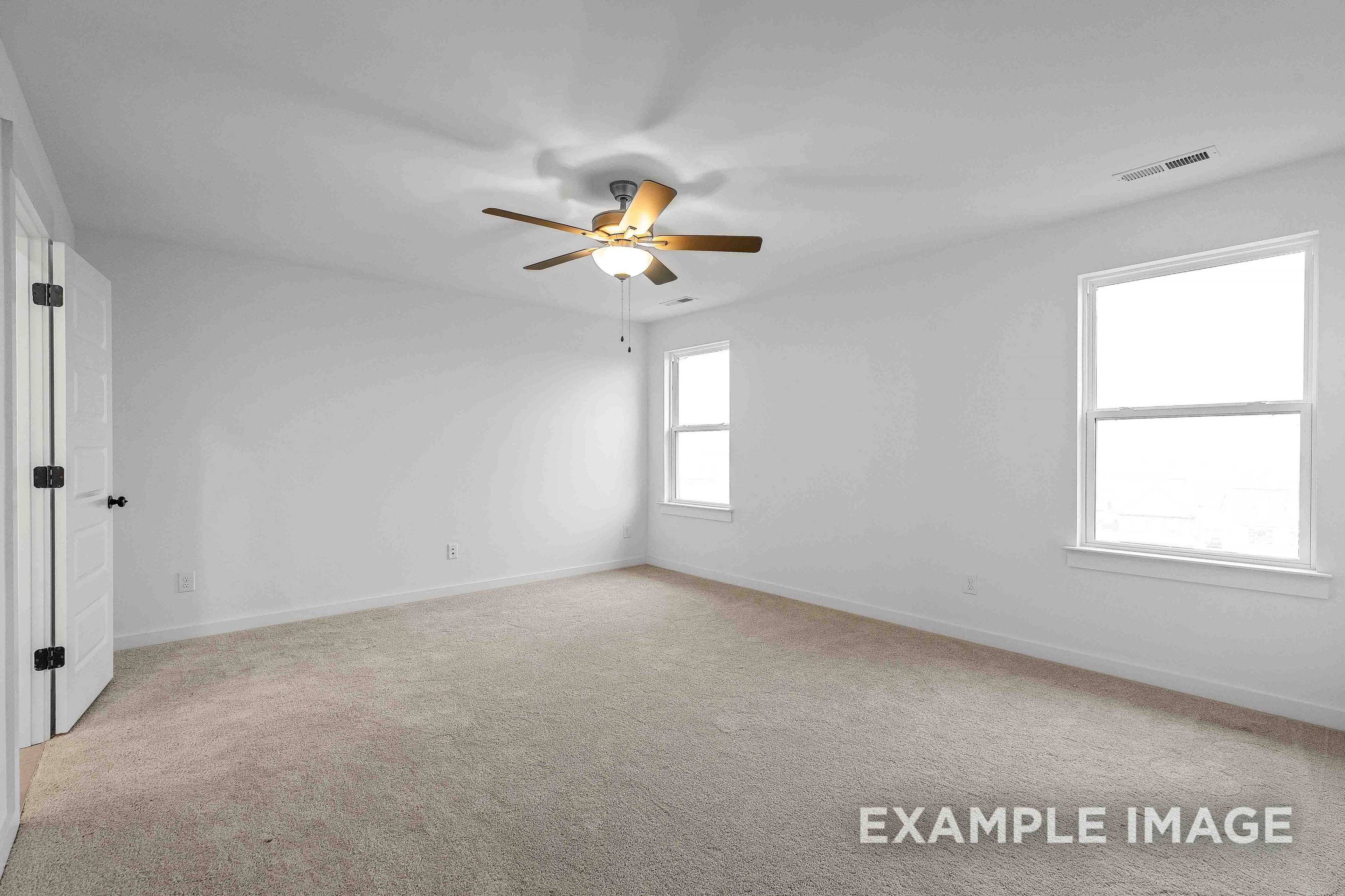 Spacious secondary bedroom in The Charleston C with white walls, beige carpet, ceiling fan, and large windows
