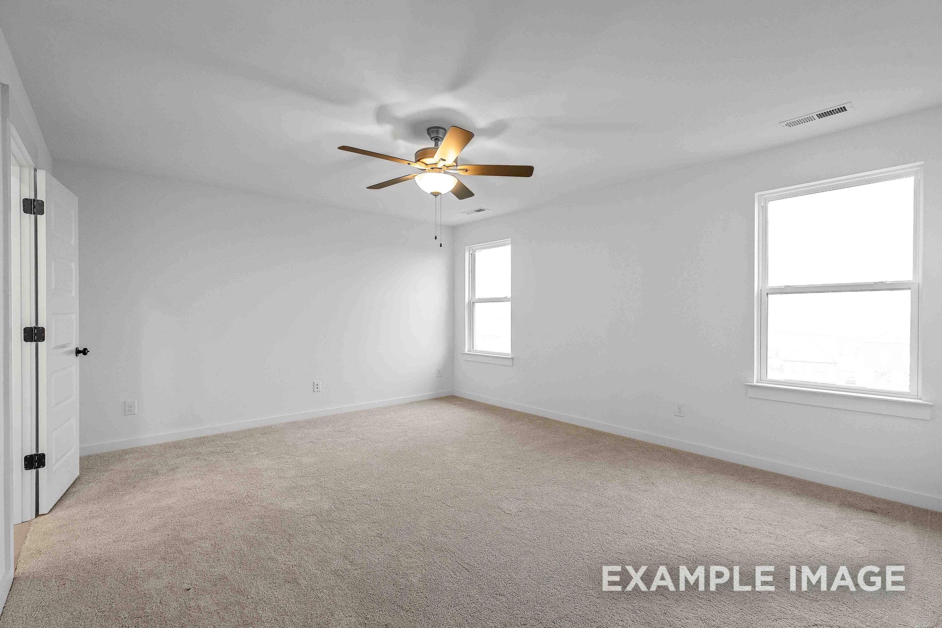 Spacious secondary bedroom in The Charleston C with white walls, beige carpet, ceiling fan, and large windows