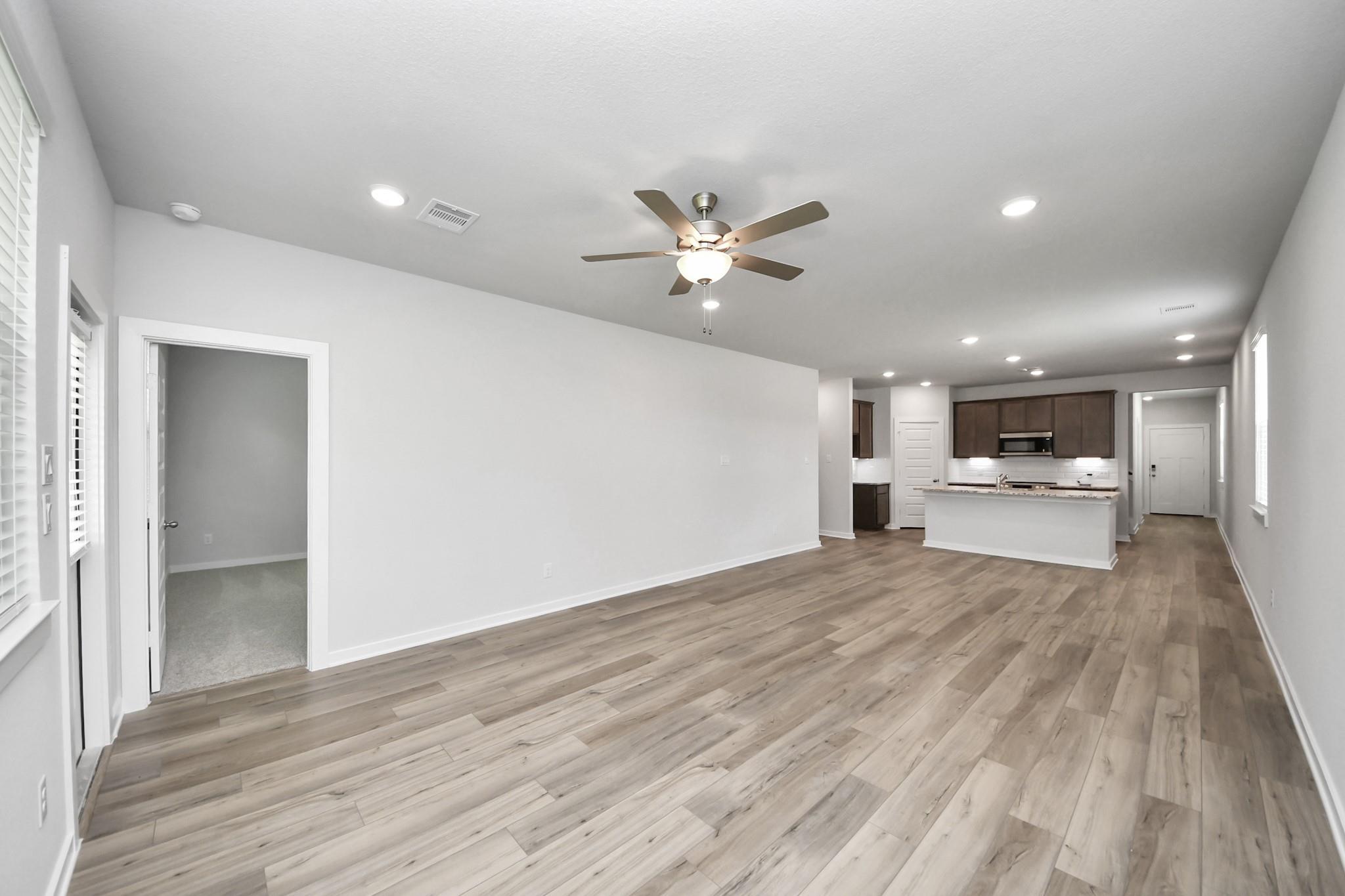 Open-concept living room with wood-look flooring in The Sabine E floor plan at Liberty Estates, Cleveland, Texas.