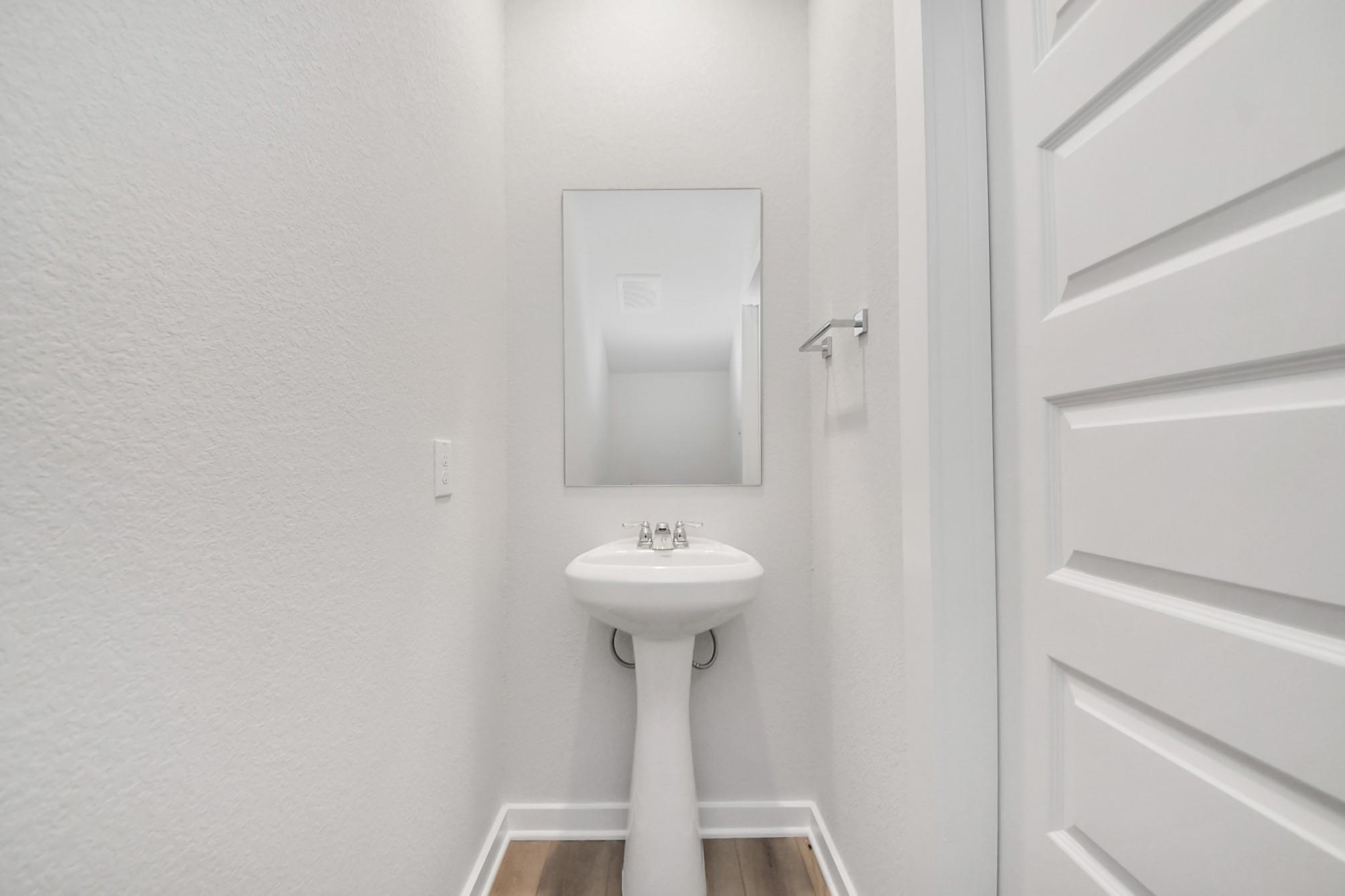 Modern half-bath with pedestal sink and wall mirror in The Blanco E floor plan at Caney Creek Place, Conroe, Texas.