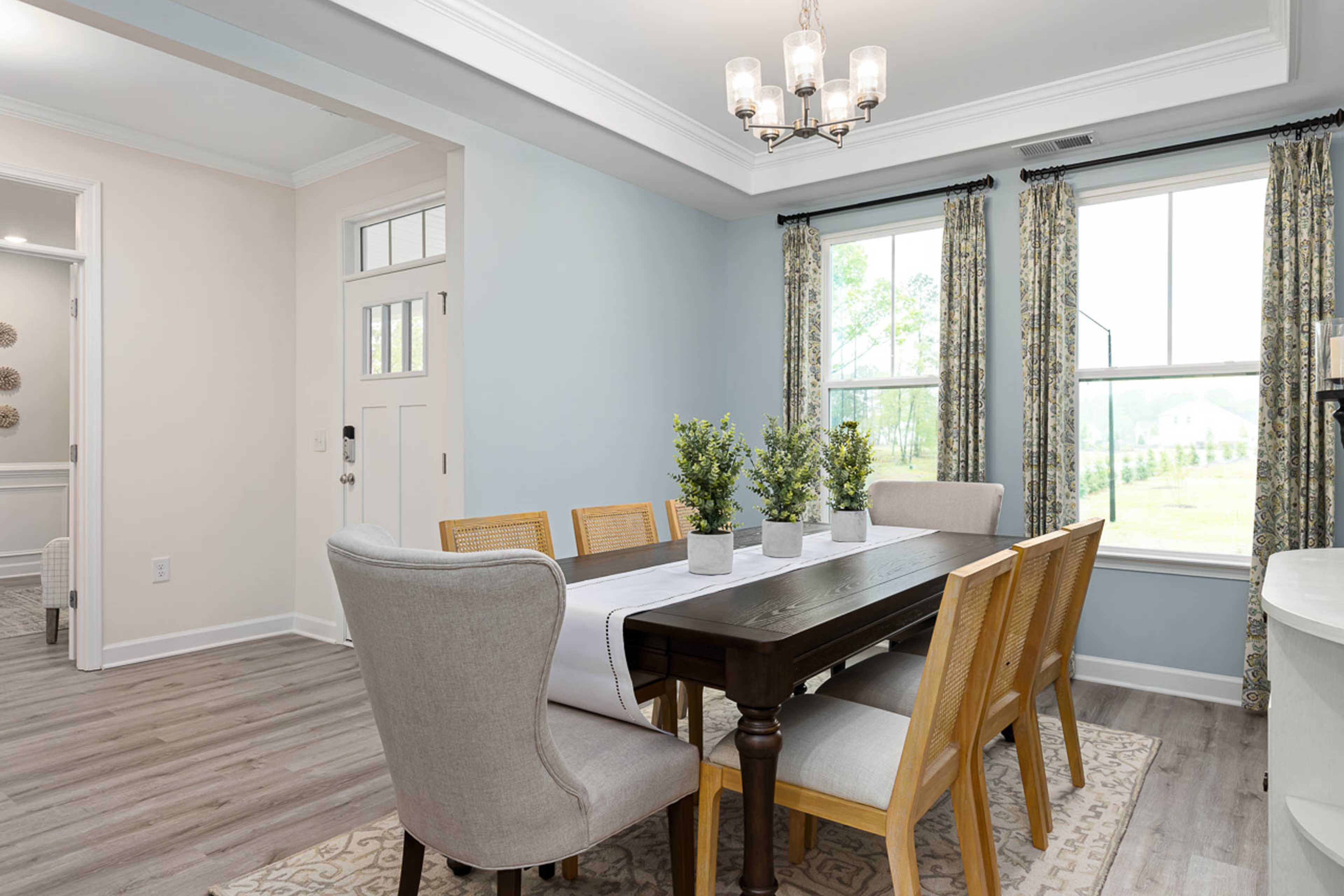 Elegant dining room at Weatherford East in Angier NC with wooden table, upholstered chairs, chandelier, plants, and large curtained windows
