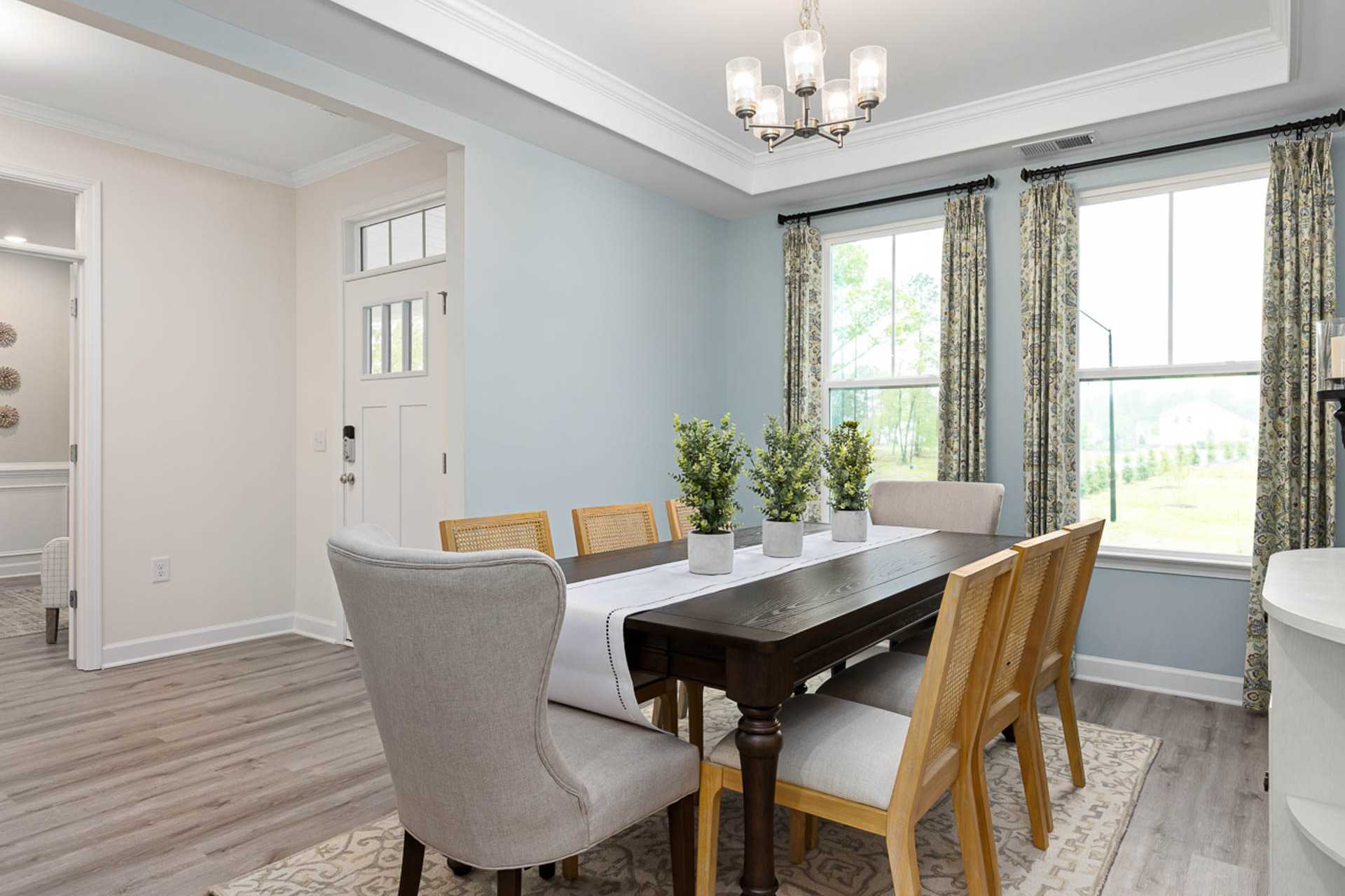Elegant dining room at Weatherford East in Angier NC with wooden table, upholstered chairs, chandelier, plants, and large curtained windows