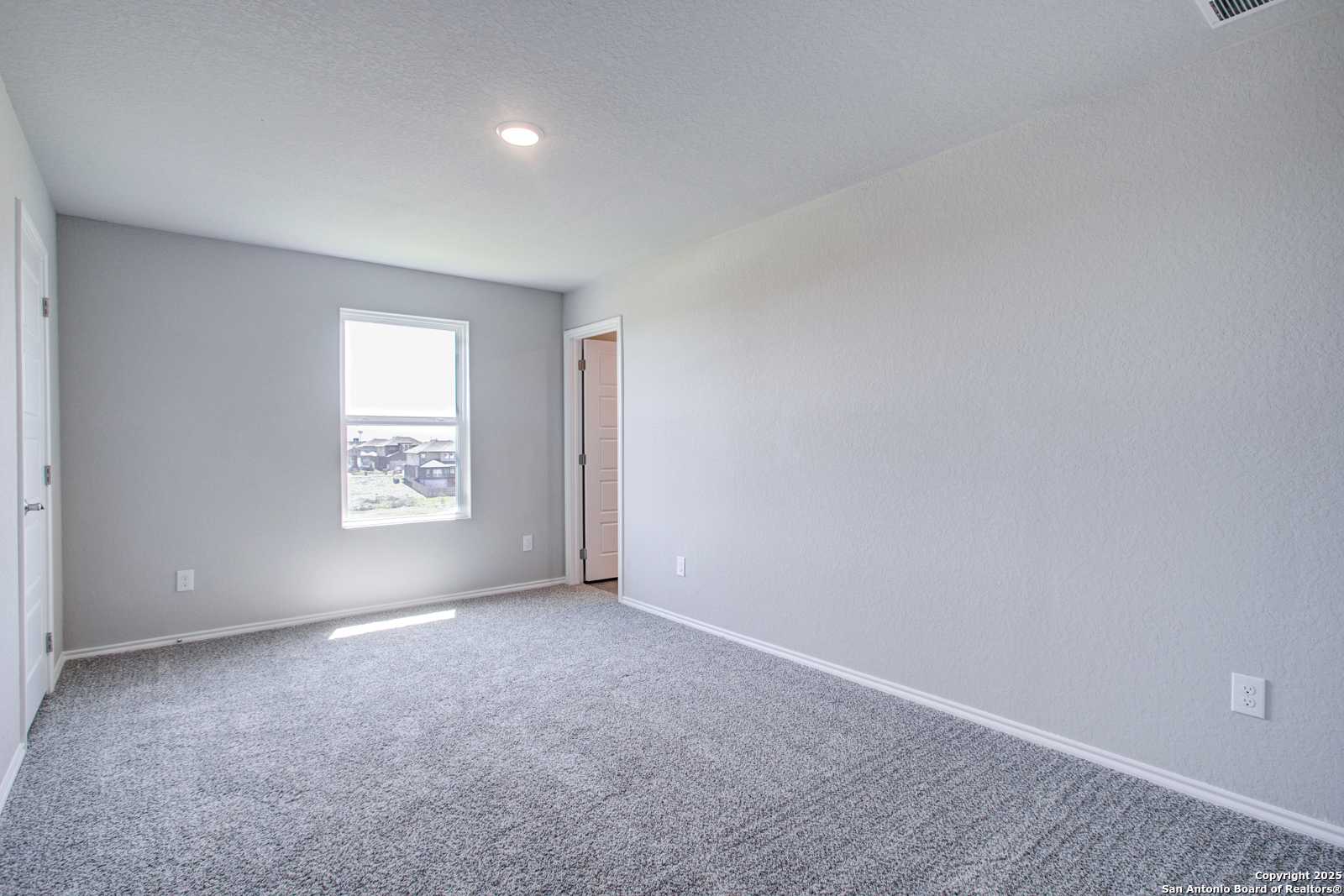Bright bedroom with light gray walls, large window, and plush carpet in Davidson Homes The Douglas G, San Antonio