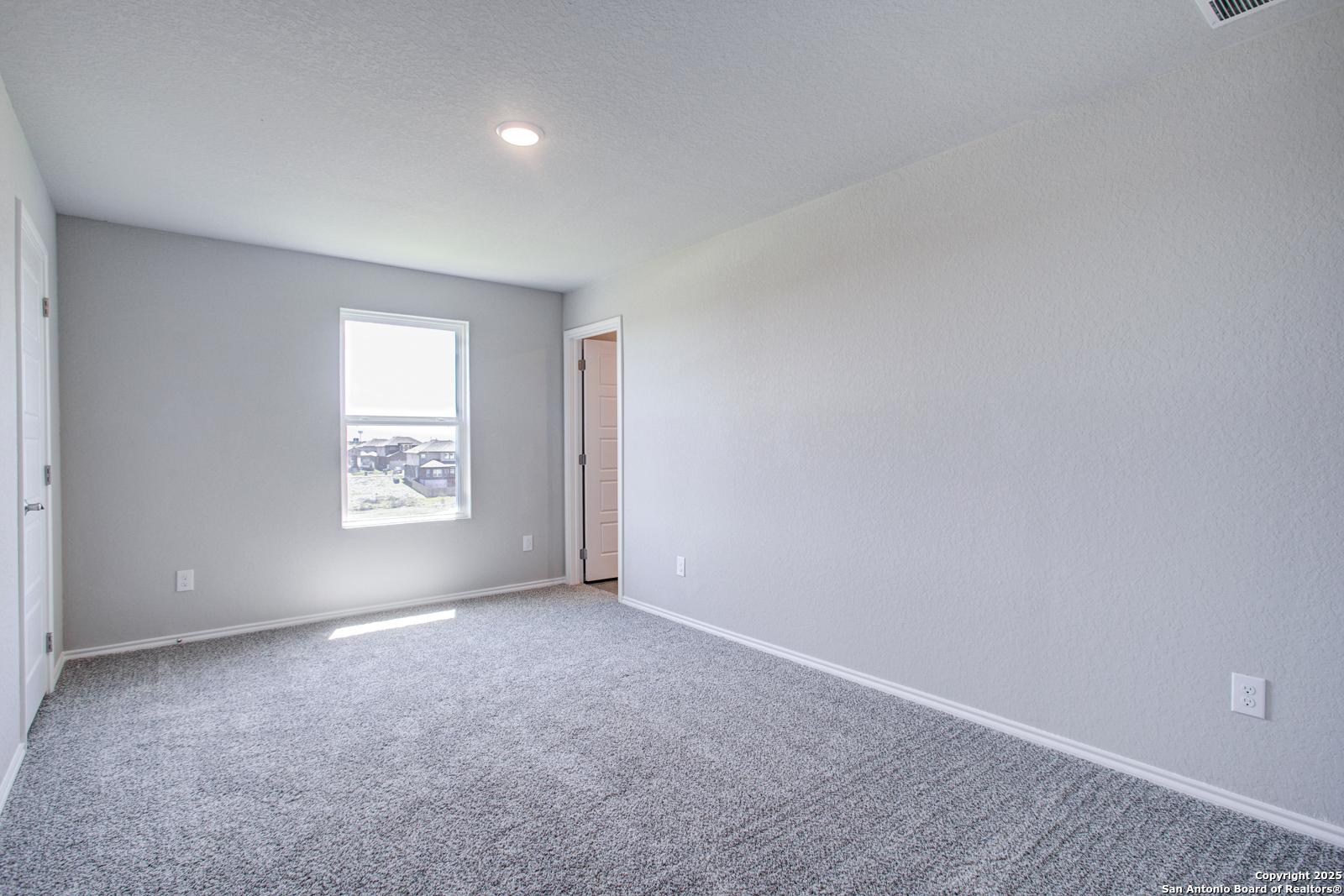 Bright bedroom with light gray walls, large window, and plush carpet in Davidson Homes The Douglas G, San Antonio