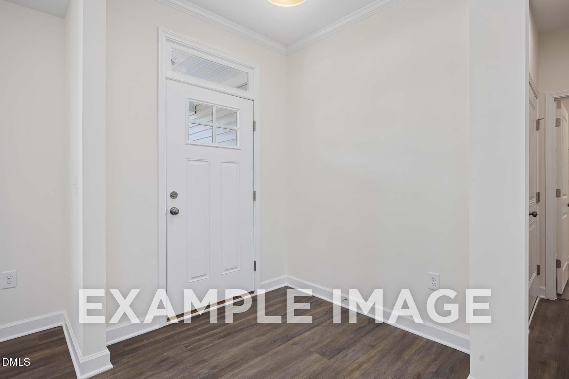 Bright entryway with white paneled door, transom window, and hardwood floors in Davidson Homes The Ash B, Zebulon, NC