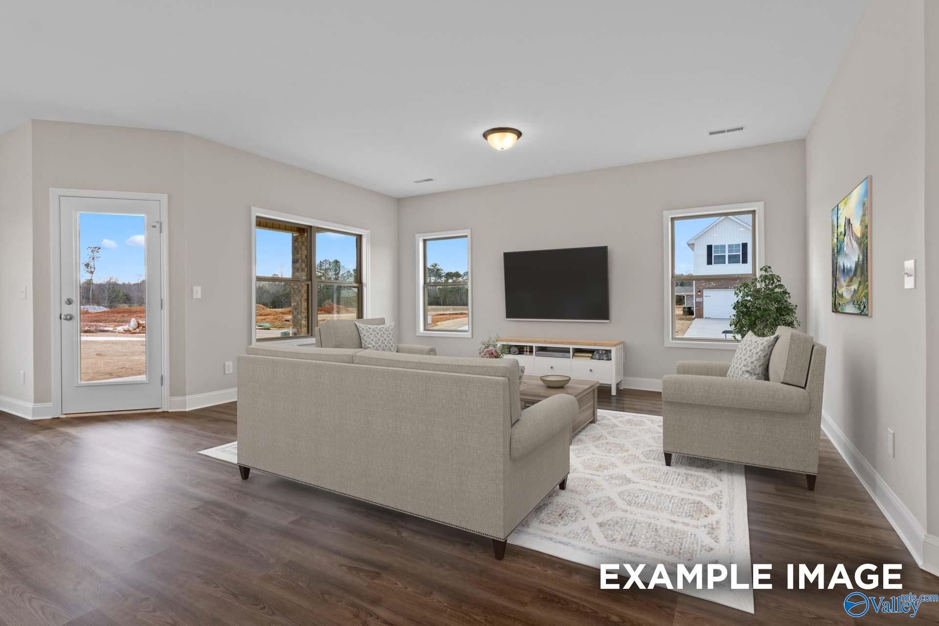 Cozy living room with beige L-shaped sofa, armchairs, mounted TV, and large windows in Davidson Homes The Everett, Meridianville, AL