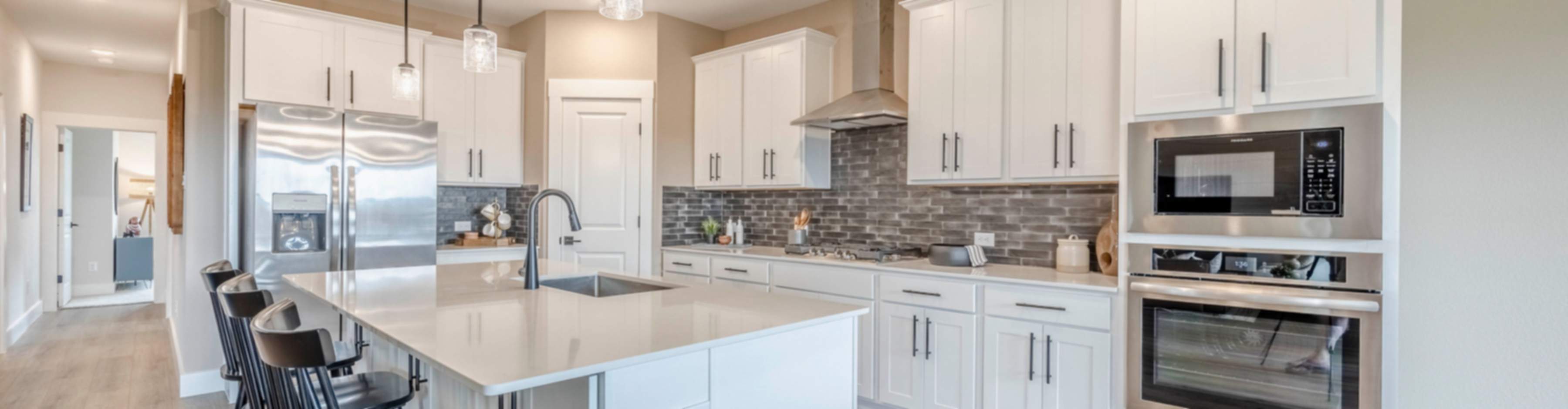 Modern white kitchen with quartz island, bar stools, stainless appliances in Royse City new home