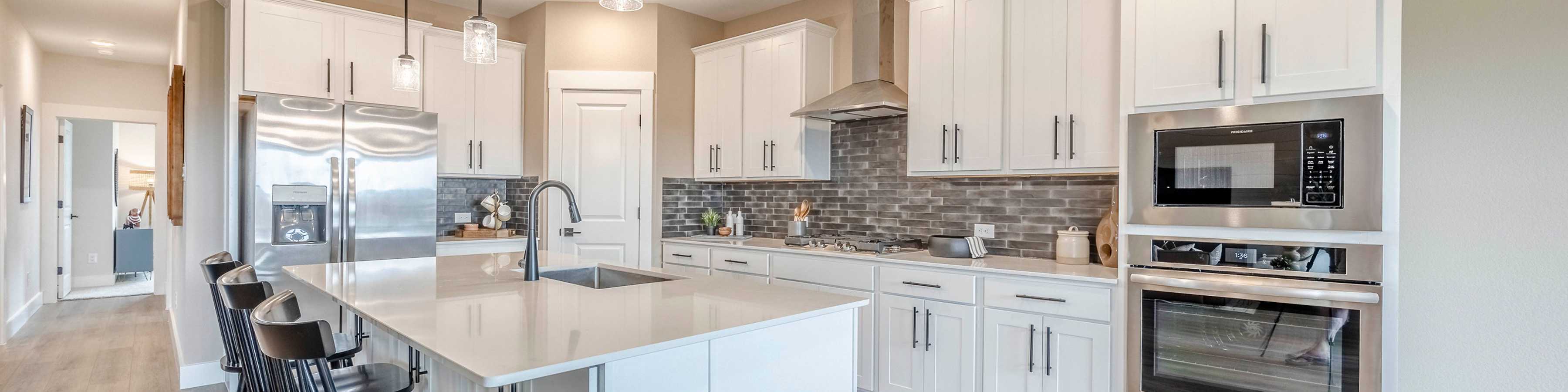 Modern white kitchen with quartz island, bar stools, stainless appliances in Royse City new home