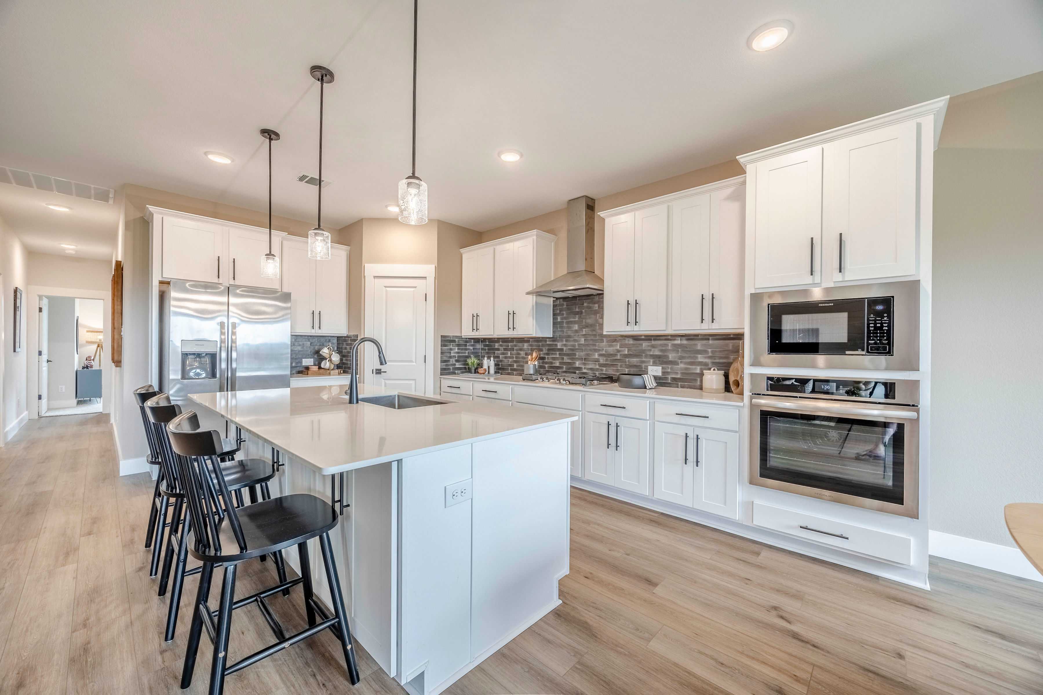 Spacious modern kitchen in The Rockford featuring white shaker cabinets, large quartz island, stainless steel appliances, and open wood-floor layout