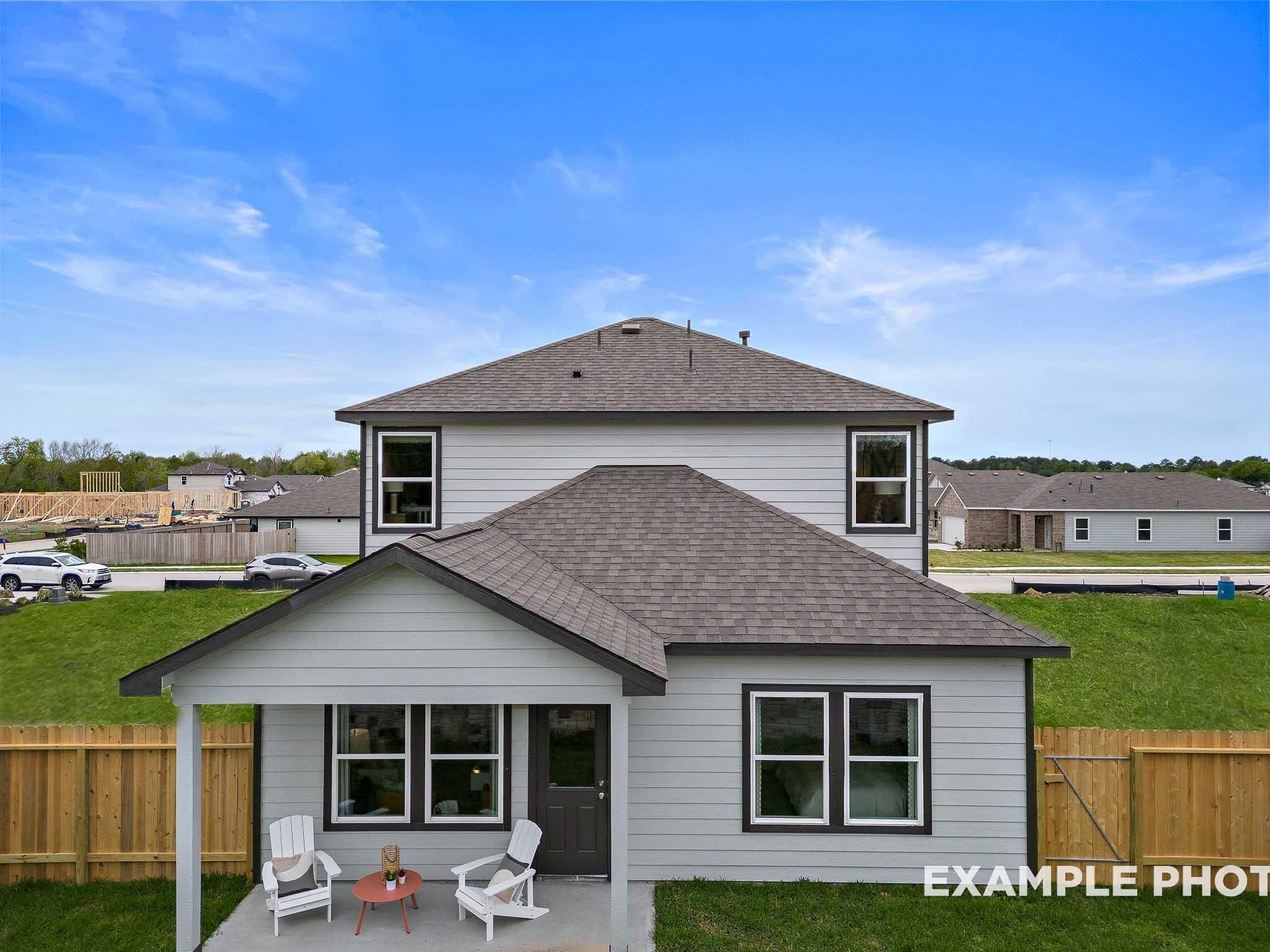 Two-story Sabine F home exterior with front porch, Adirondack chairs, and lush lawn in Windmill Estates, Magnolia, Texas