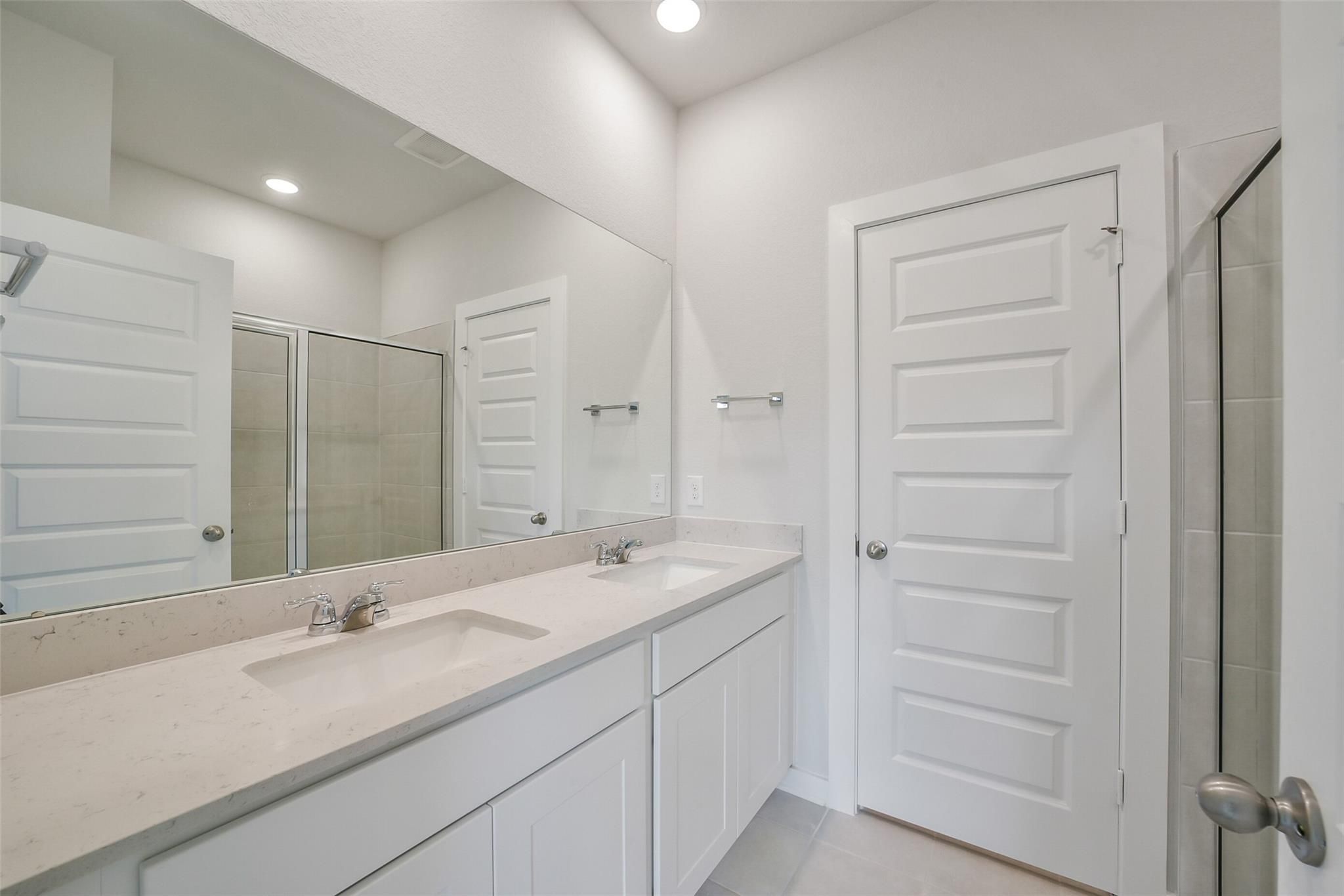 Modern master bathroom featuring double vanity sinks, oversized mirrors, and glass shower in Davidson Homes The Frio F, Conroe, Texas