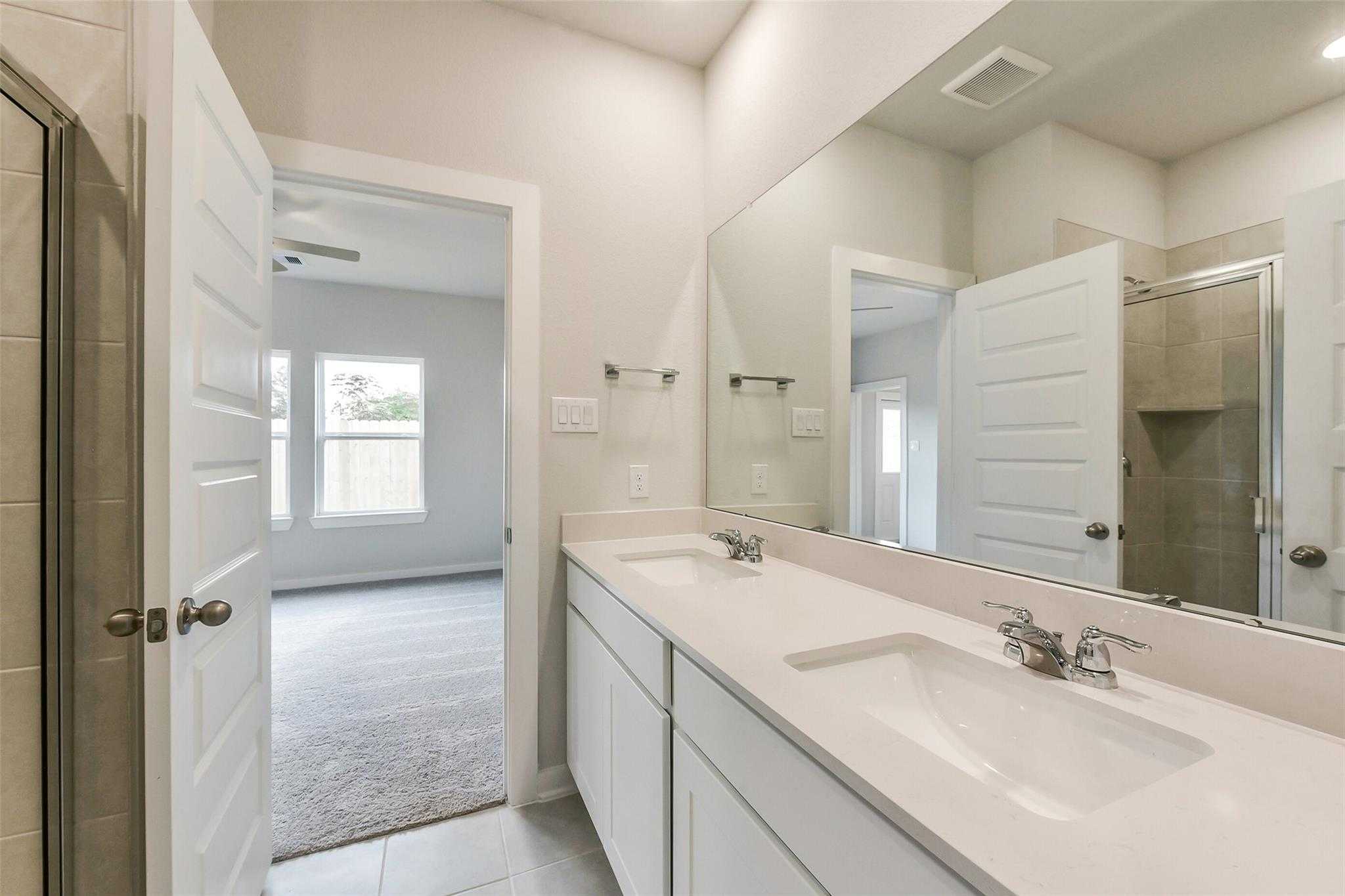 Modern master bathroom featuring double vanity sinks, large mirror, and glass shower in Davidson Homes The Frio G, Dayton, Texas