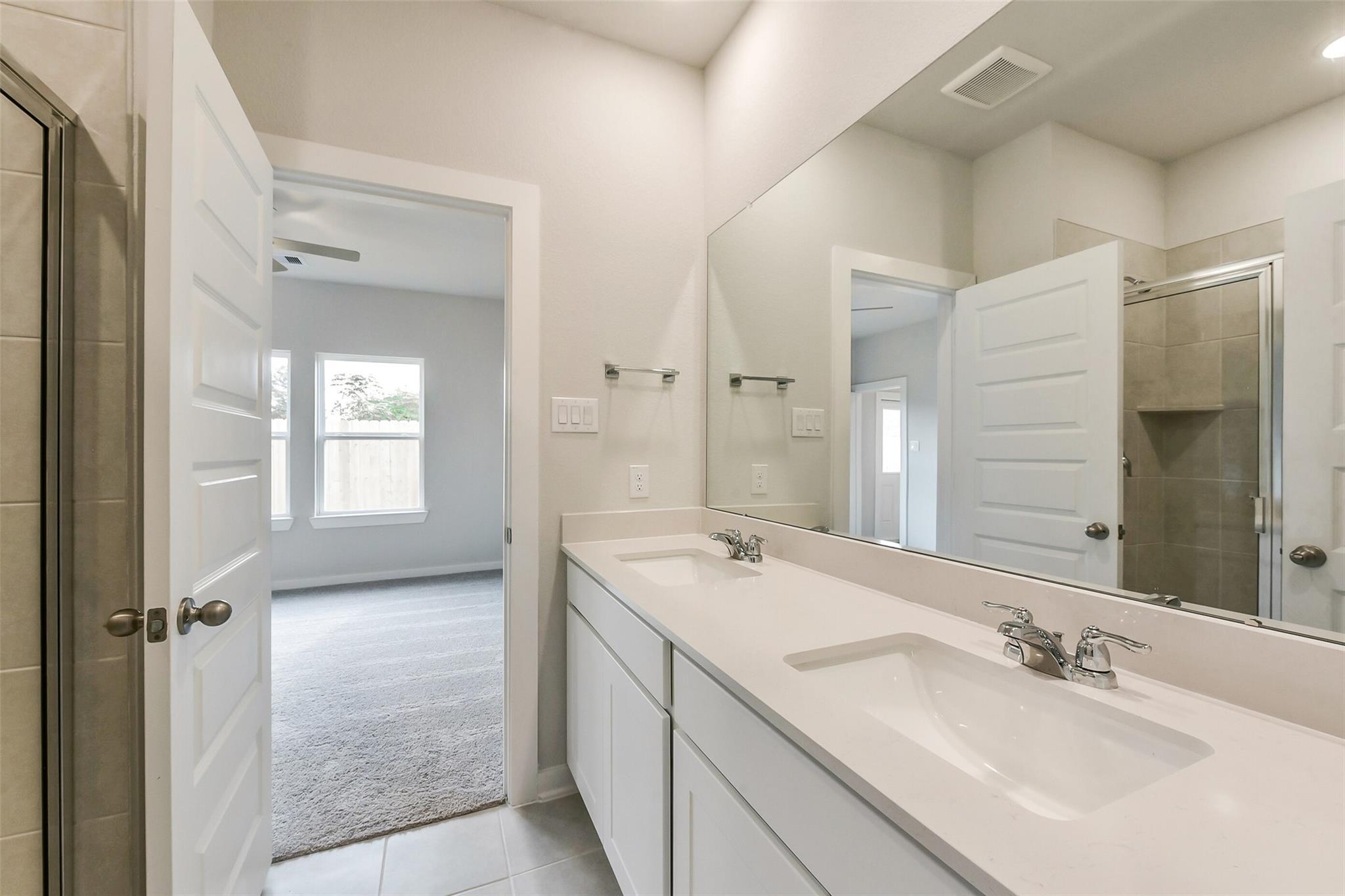 Modern master bathroom with double vanity, large mirror, glass shower, and bedroom access in Davidson Homes The Frio G, Dayton Texas