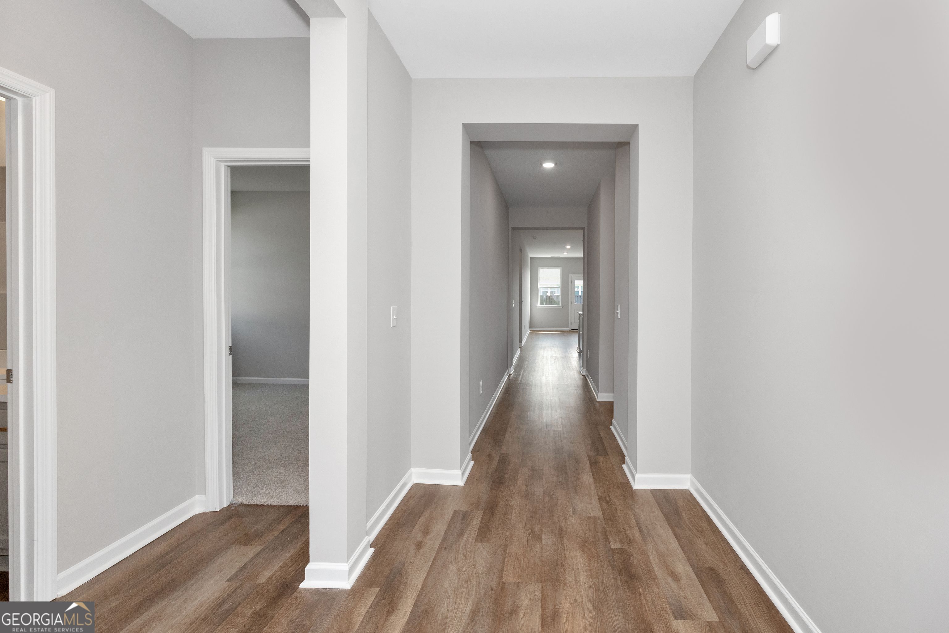 Spacious hallway with light gray walls, luxury vinyl plank floors, and open doorways in Evermore Homes The Luna, Perry, Georgia