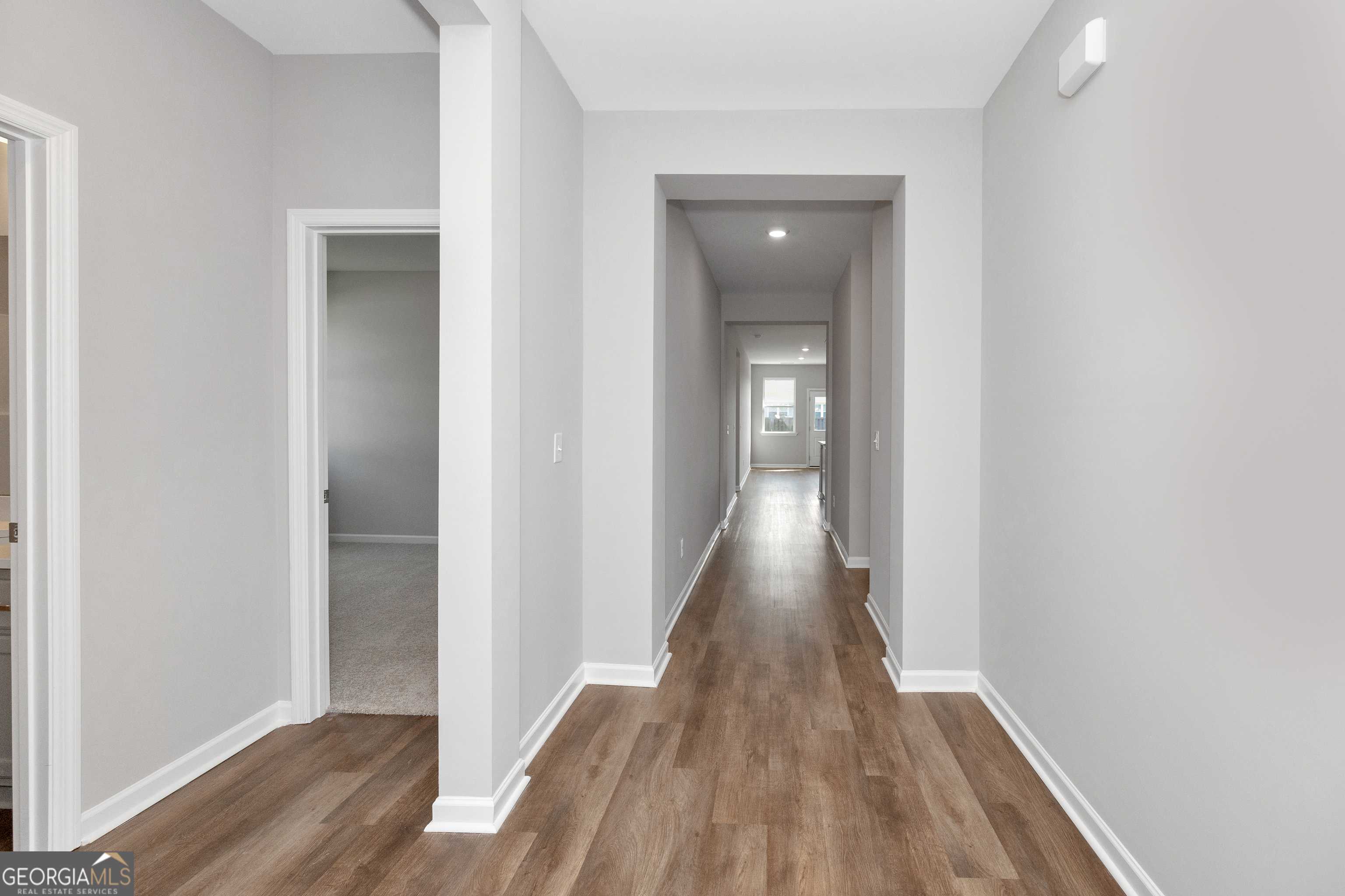Spacious hallway with light gray walls, luxury vinyl plank floors, and open doorways in Evermore Homes The Luna, Perry, Georgia