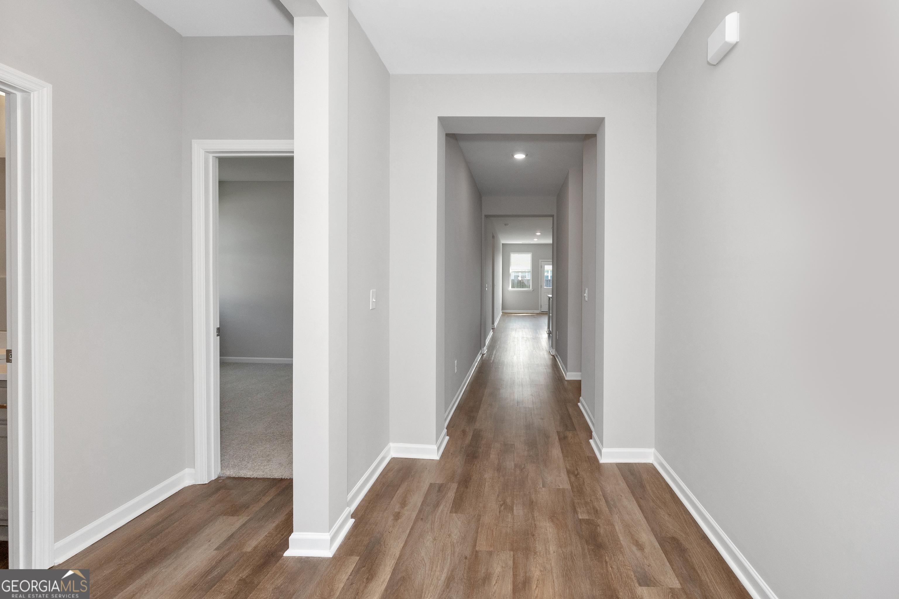 Elegant hallway with light gray walls, wood-tone luxury vinyl plank floors, and open archway in The Luna 4-bedroom home, Ivy Glen, Perry, Georgia