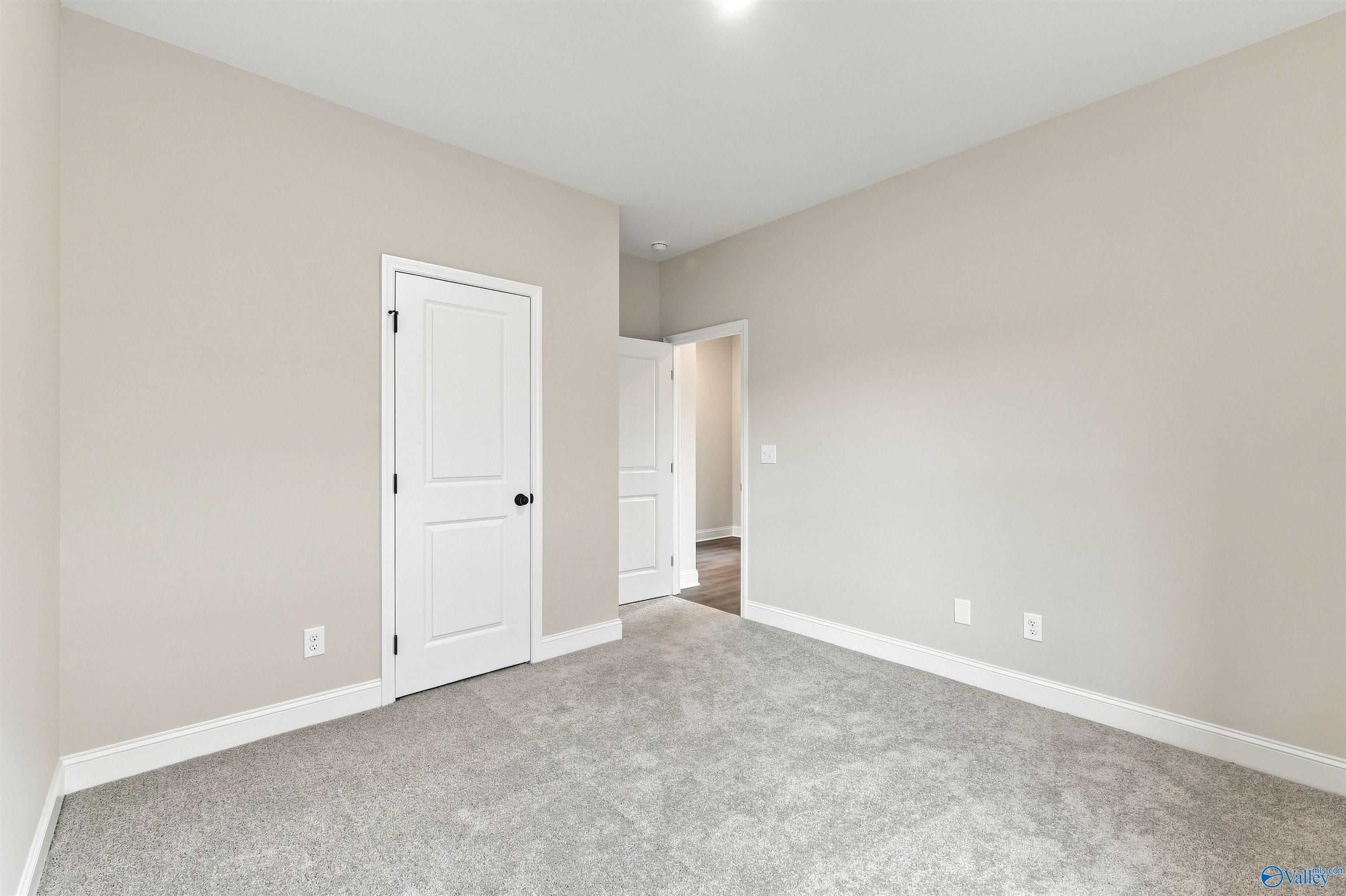 Spacious carpeted bedroom with neutral walls and white doors in Davidson Homes Franklin C plan, The Meadows, Athens, Alabama