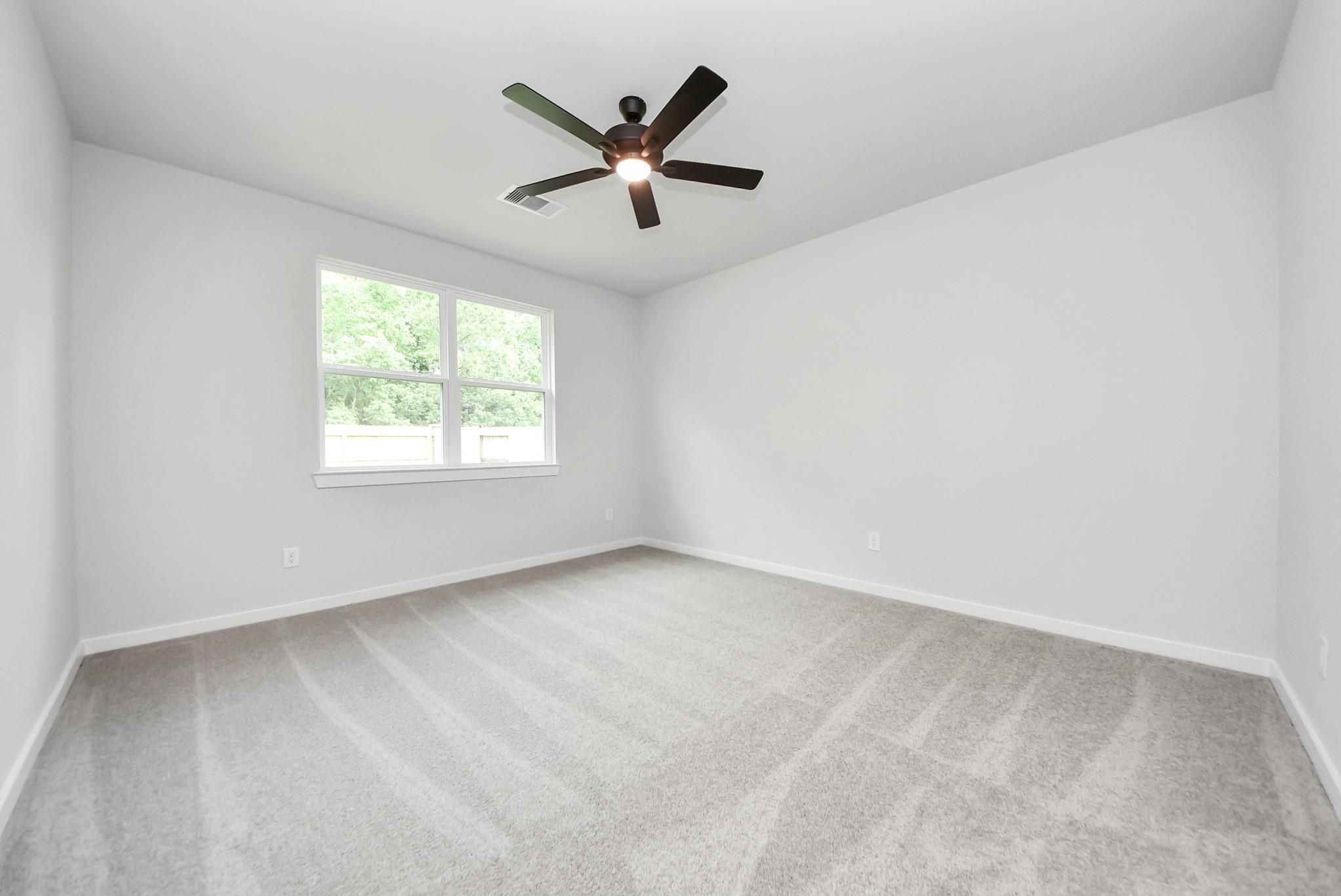 Spacious carpeted bedroom with ceiling fan in The Daphne F floor plan at Sundance Cove, Crosby, Texas.