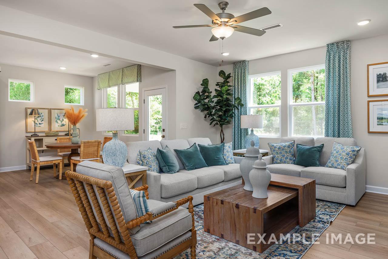 Bright open-concept living room in The Willow C-BF by Davidson Homes featuring gray sofas, teal accents, and wood floors.
