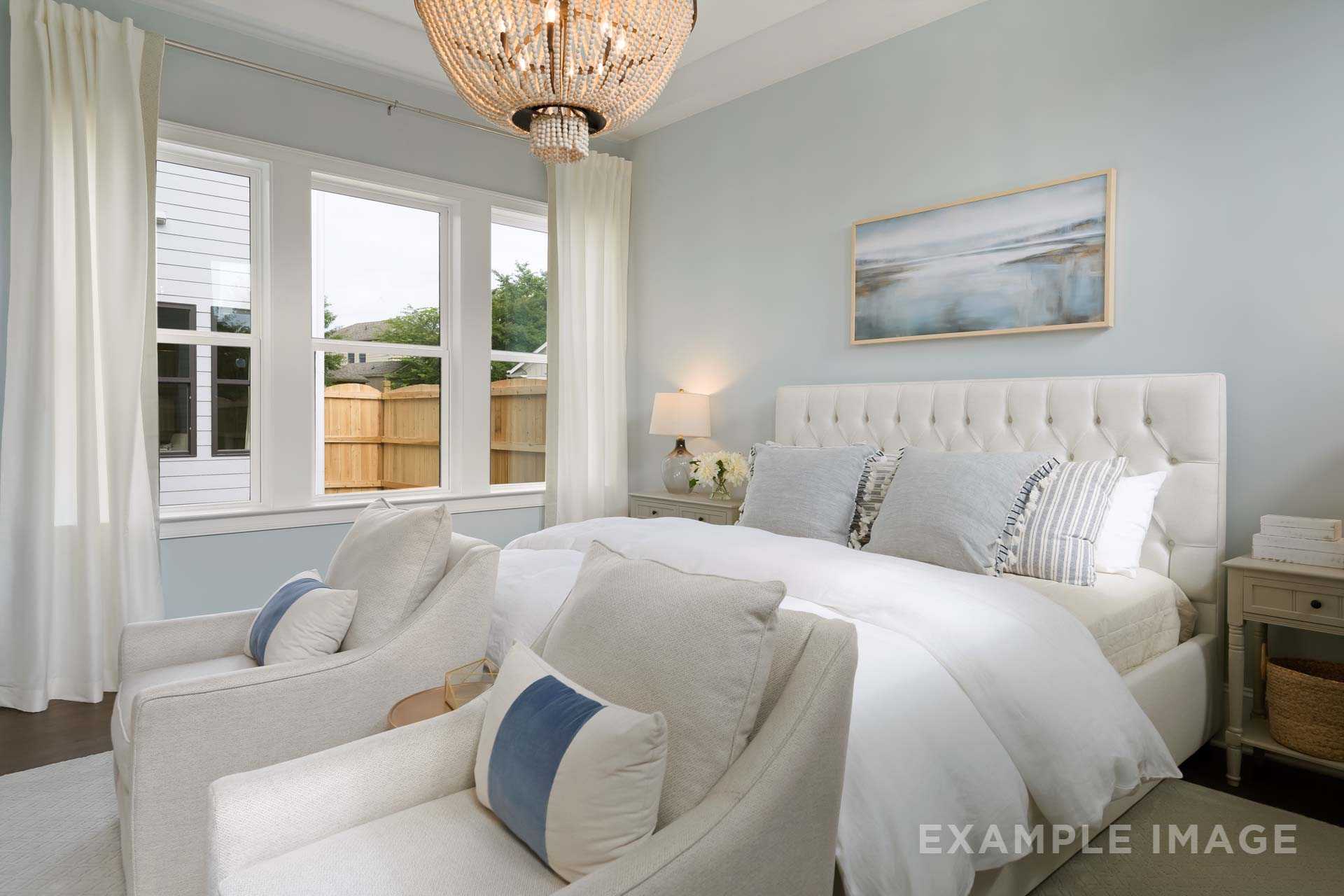 Spacious master bedroom in The Seaside by Davidson Homes featuring white tufted bed, armchairs, coastal art, and soft blue walls in Woodstock, GA