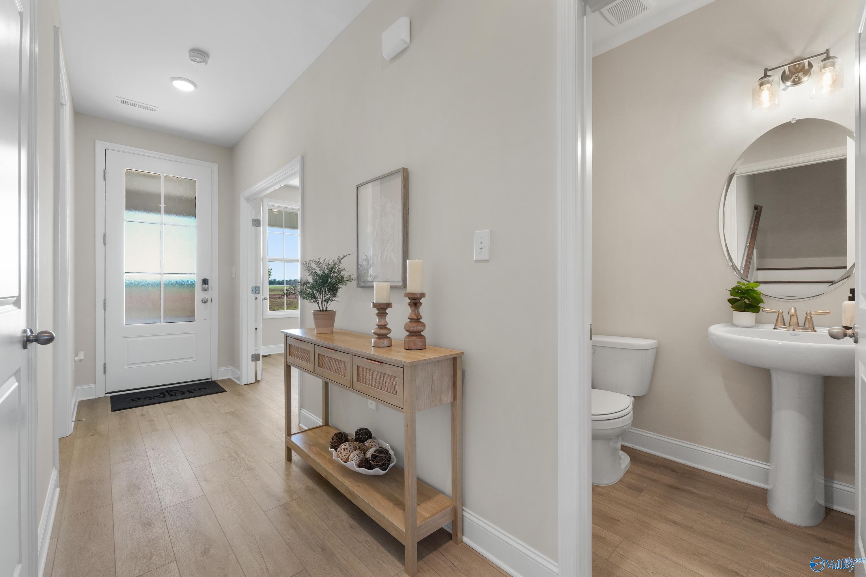 Elegant entryway with oak console table, plants, and adjacent powder room with white vanity in Davidson Homes The Rockford B, Toney, Alabama