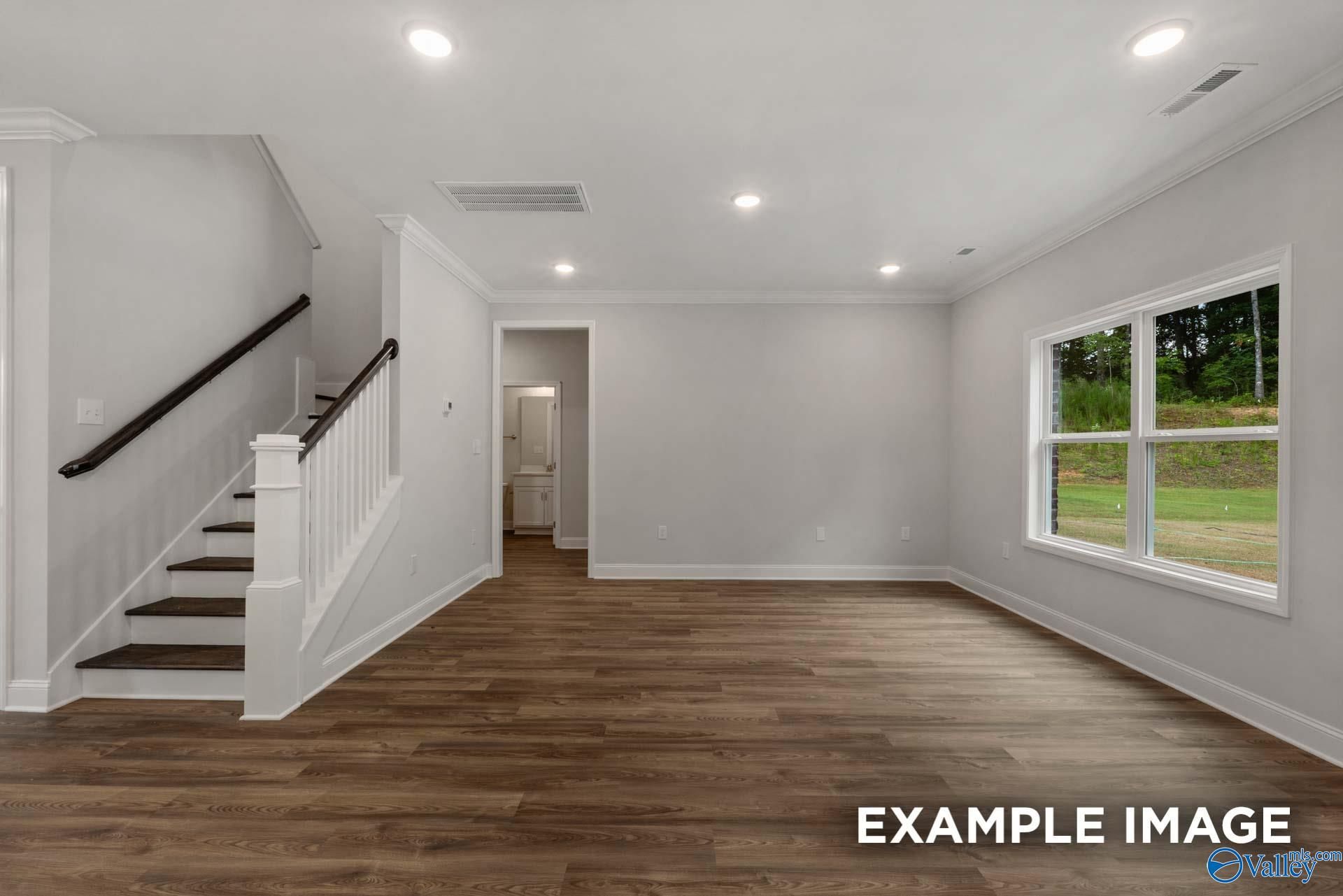 Spacious two-story foyer with white wooden staircase, hardwood floors, large windows to wooded backyard in The Shelby C, Arab, Alabama
