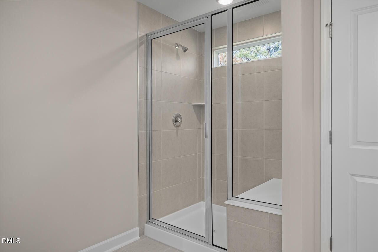 Elegant frameless glass shower with beige subway tiles, built-in niche, and clerestory window in Davidson Homes The Graham master bath, Fuquay-Varina, NC