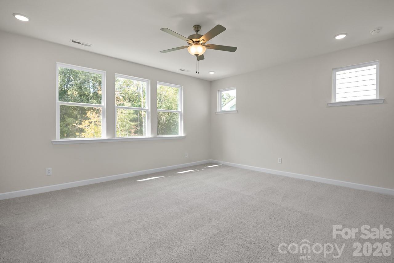 Bright upstairs bedroom with large windows, trees view, ceiling fan, and gray carpet in Davidson Homes The Beech B, Belmont NC