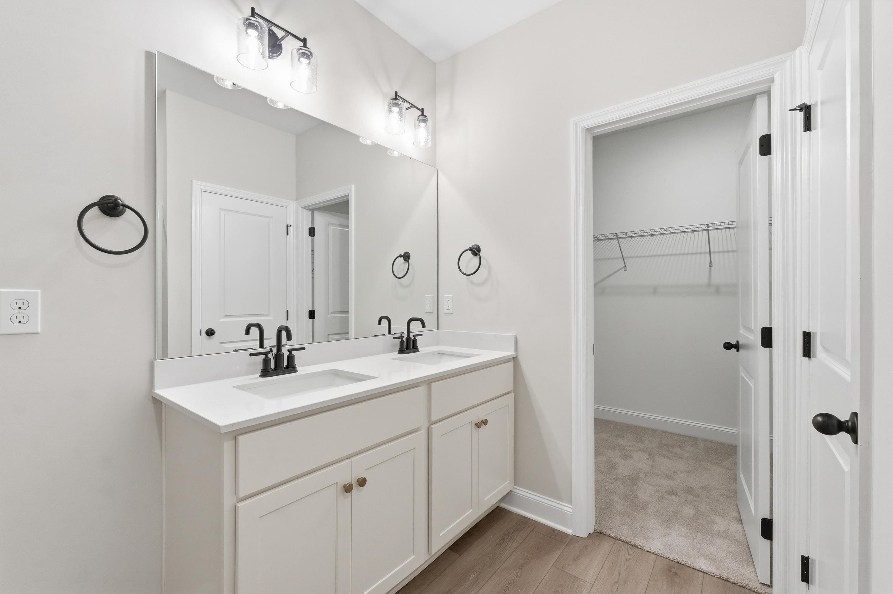 Master bathroom in The Glen A featuring dual vanity, modern black fixtures, and a spacious walk-in closet.