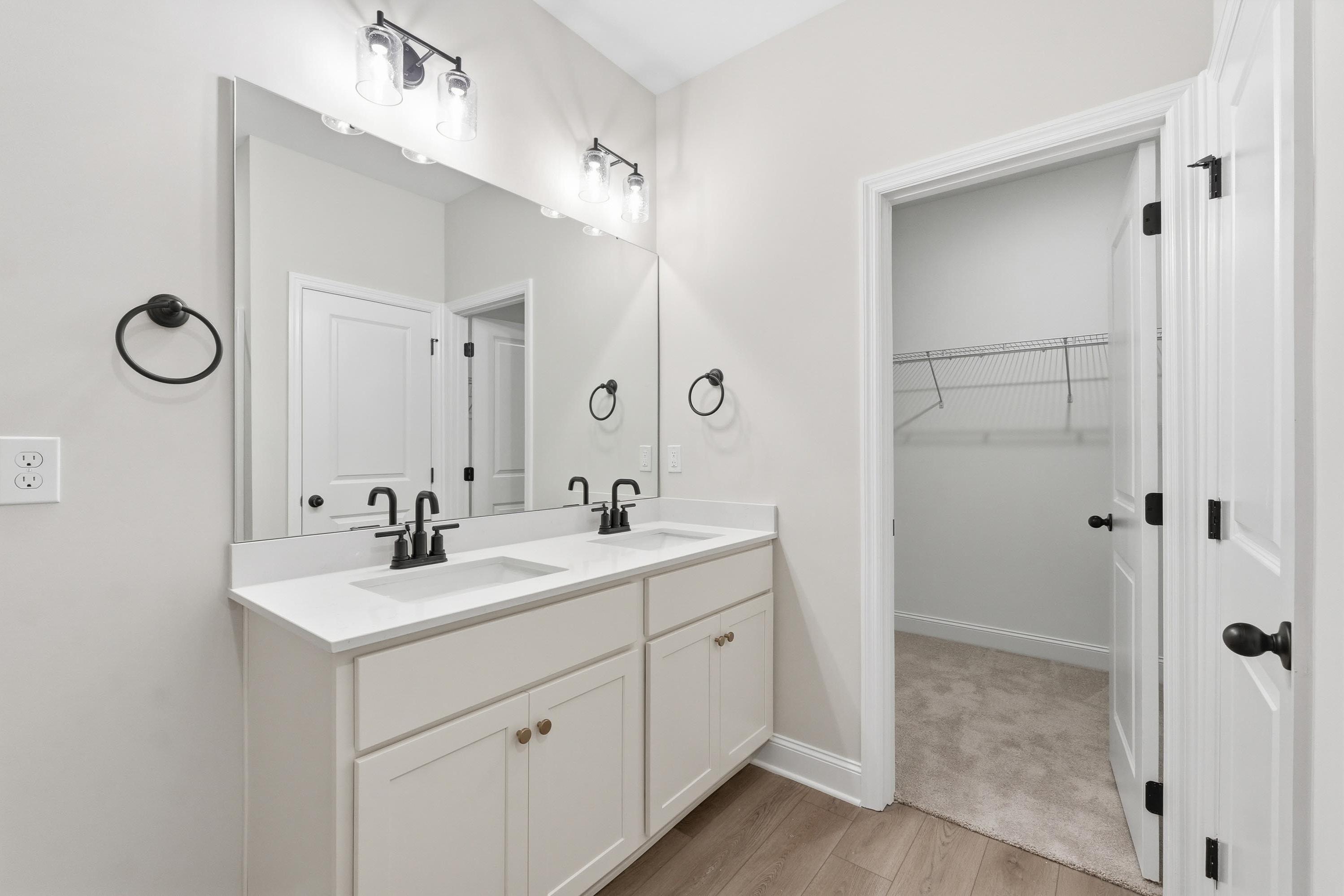 Master bathroom in The Glen A featuring dual vanity, modern black fixtures, and a spacious walk-in closet.