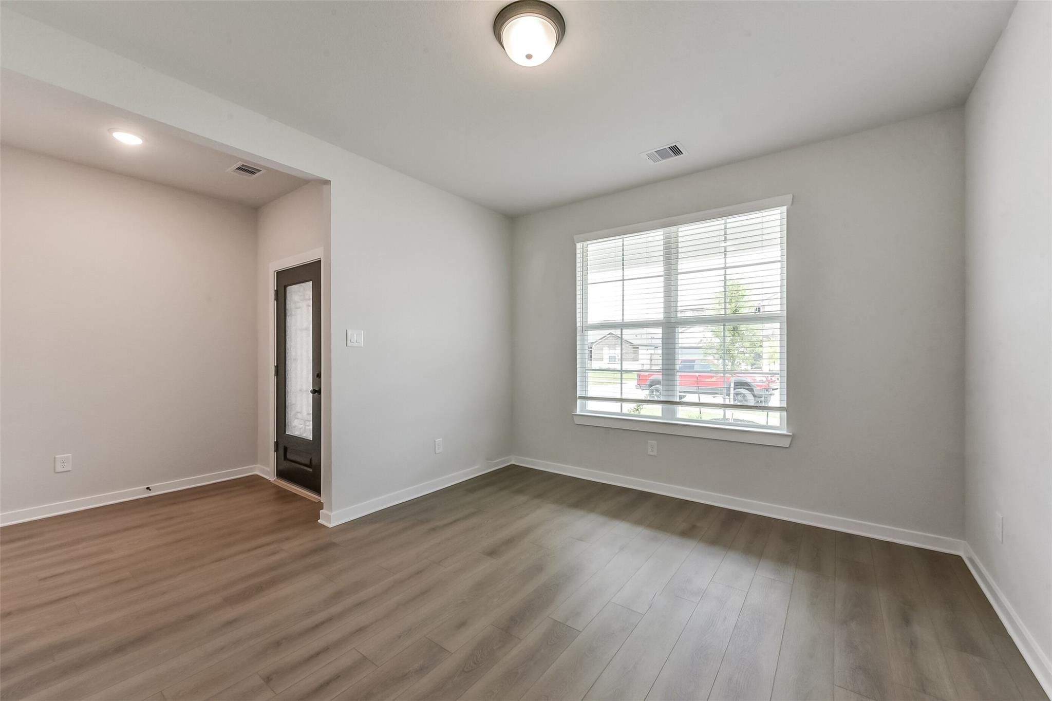 Bright interior room with gray walls, luxury vinyl plank flooring, large window with blinds, and garage door entry in Davidson Homes The Everett C, Crosby, Texas