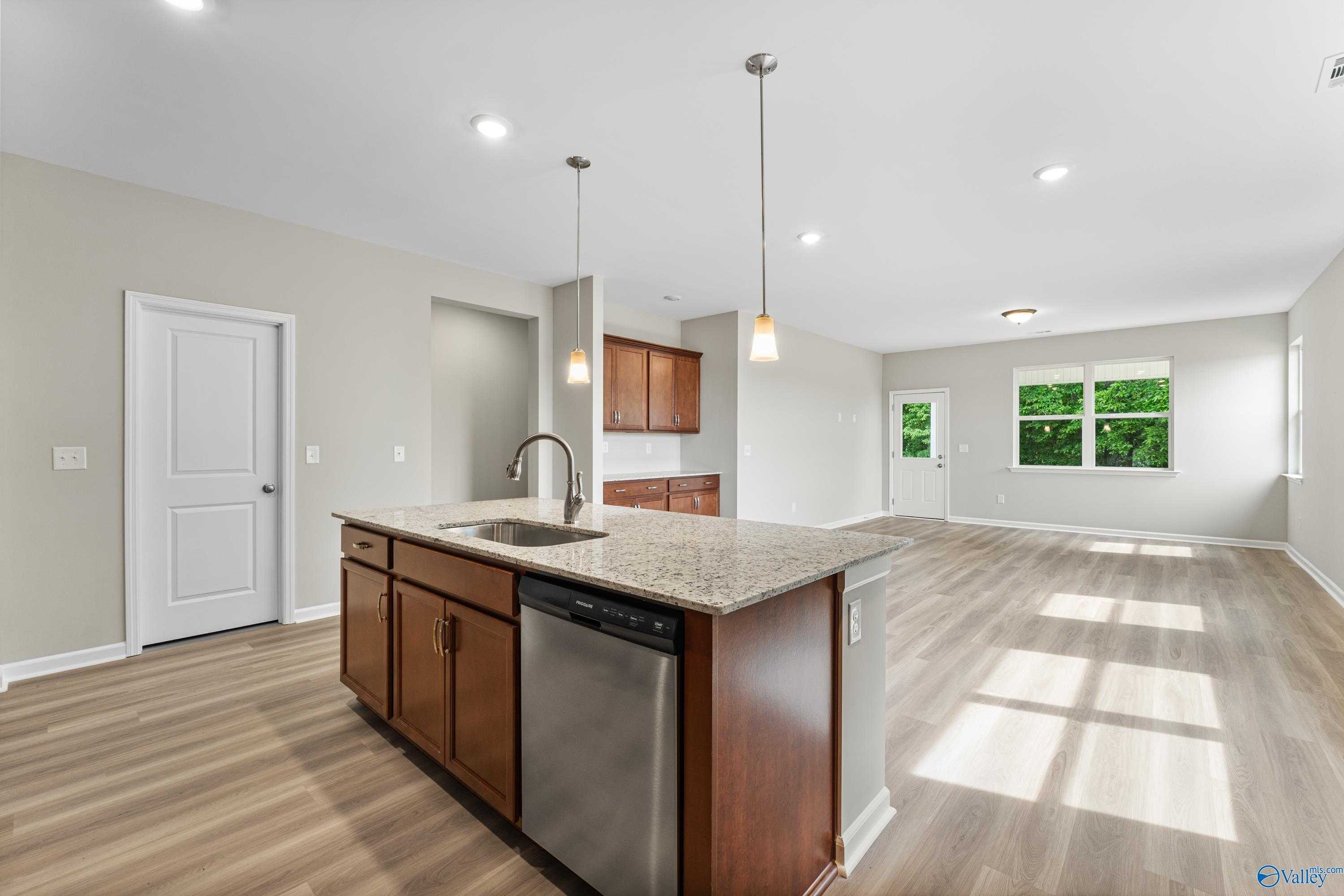 Open-concept kitchen with granite island, wood cabinets, stainless dishwasher, and hardwood floors in The Aurora 4-bedroom home, Fayetteville TN