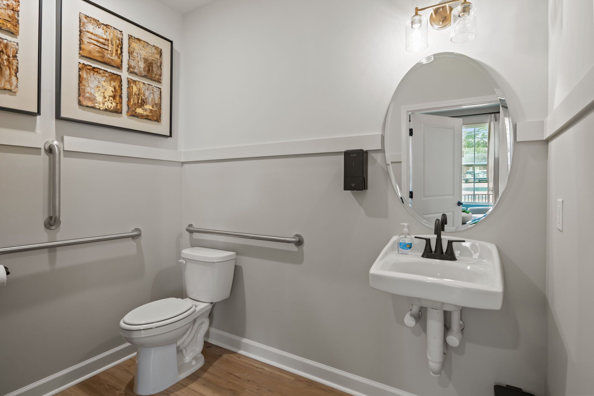 Accessible powder room in The Mitchell interior, featuring a wall-mounted sink, oval mirror, and safety grab bars.