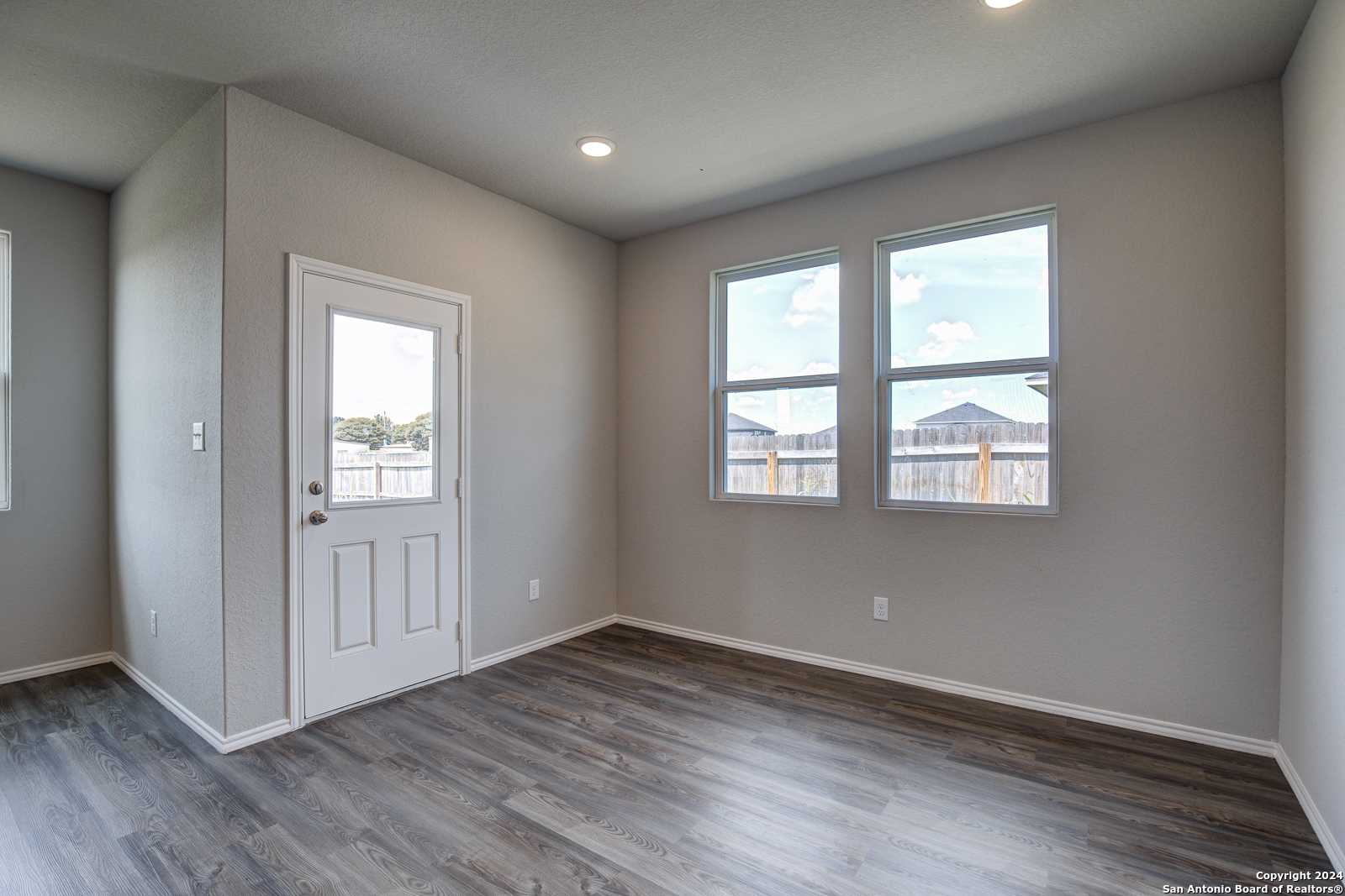 Bright secondary bedroom with large windows, gray walls, wood-look floors, and glass door in The Daphne J home, Seguin, Texas