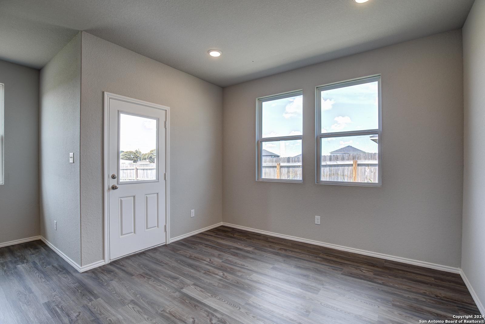 Bright secondary bedroom with large windows, gray walls, wood-look floors, and glass door in The Daphne J home, Seguin, Texas
