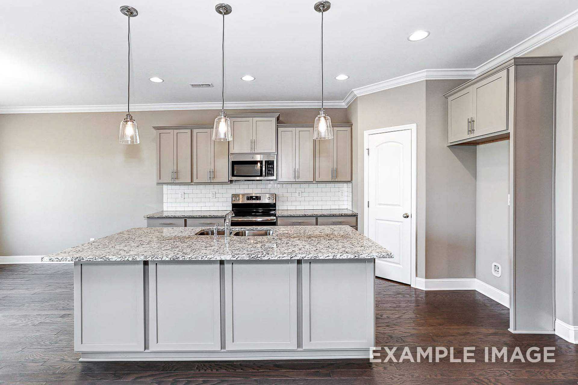 Spacious kitchen in The Montgomery B with white cabinetry, granite island, stainless appliances, and pendant lighting