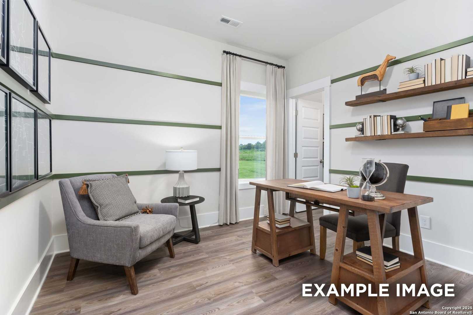 Cozy home office with wooden desk, built-in bookshelves, gray armchair, and window overlooking green field in Davidson Homes The Daphne H, Seguin Texas