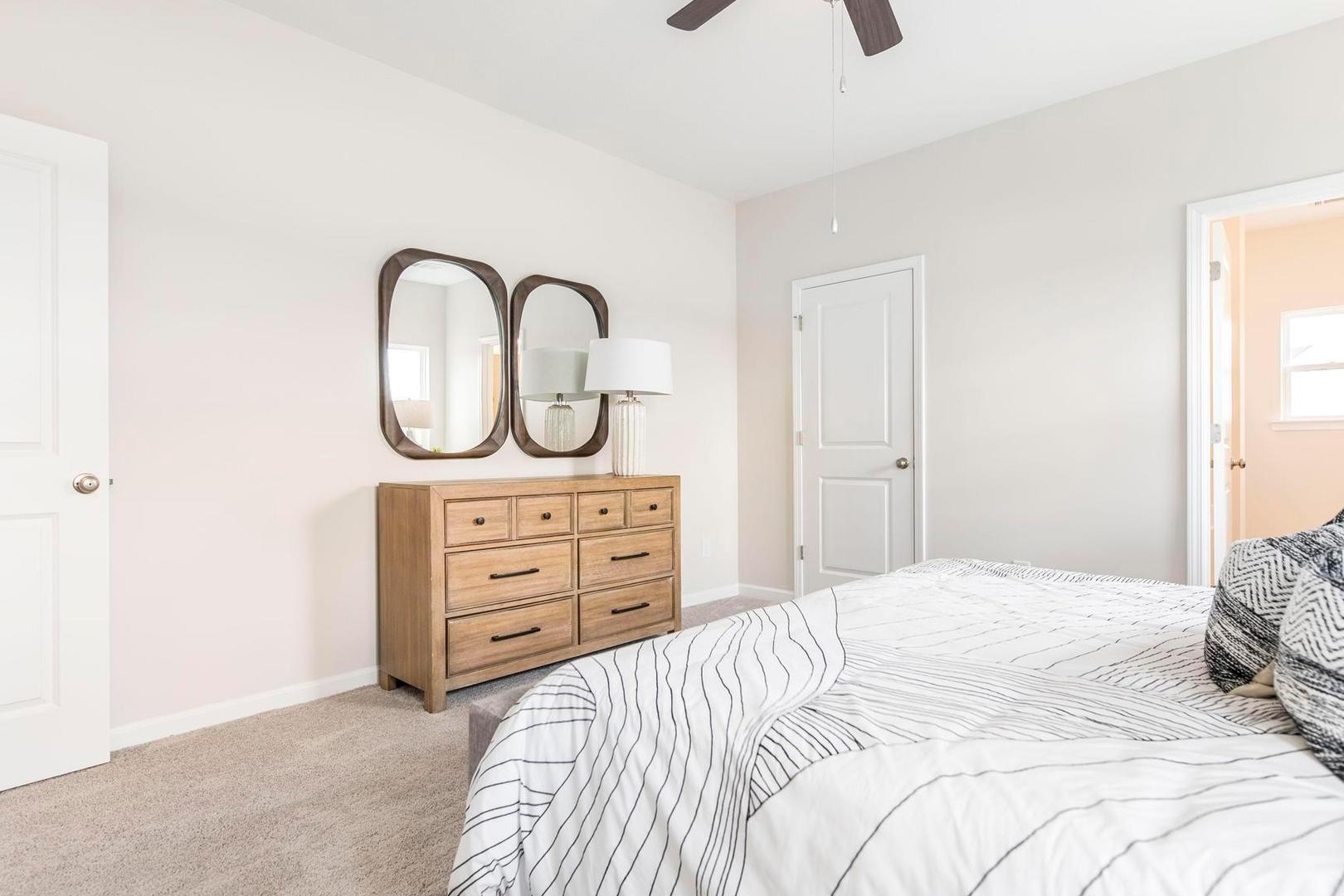 Spacious primary bedroom at Cape Reserve at Donahue Ridge in Auburn AL with king bed, wooden dresser, mirrors, and ceiling fan