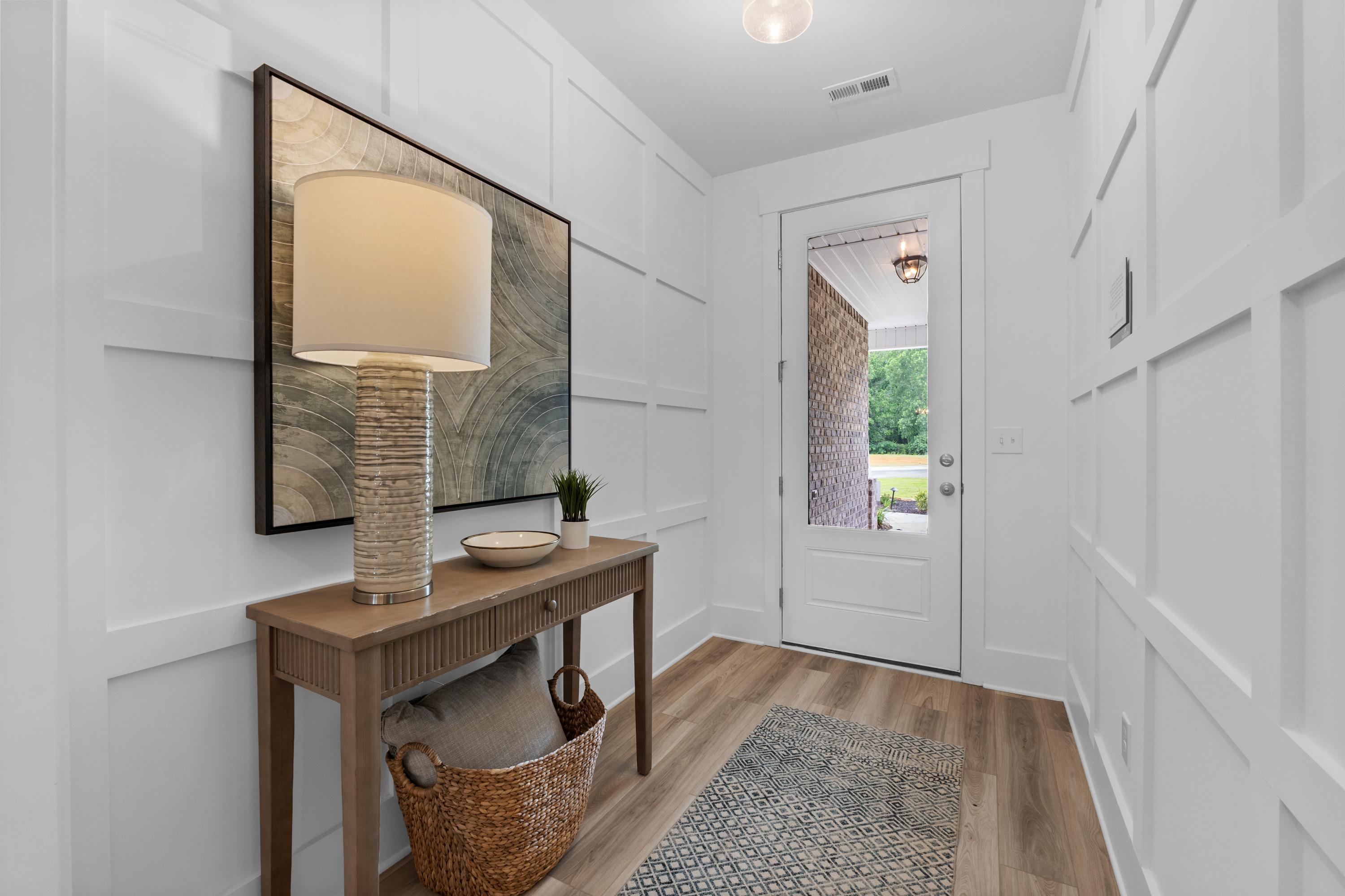 Spacious entryway in The Highlands Arab Alabama home with white shiplap walls, wooden console table, tall lamp, and glass door to lush backyard