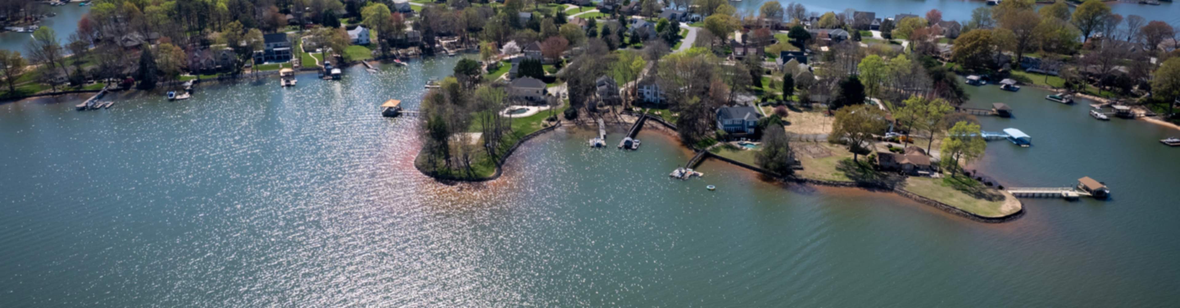 Aerial view of serene waterfront new home community in Davidson, featuring lakeside homes, docks, boats, and lush greenery