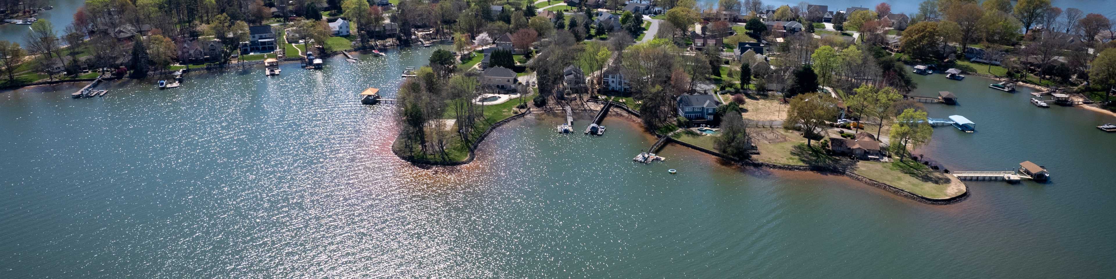 Aerial view of serene waterfront new home community in Davidson, featuring lakeside homes, docks, boats, and lush greenery